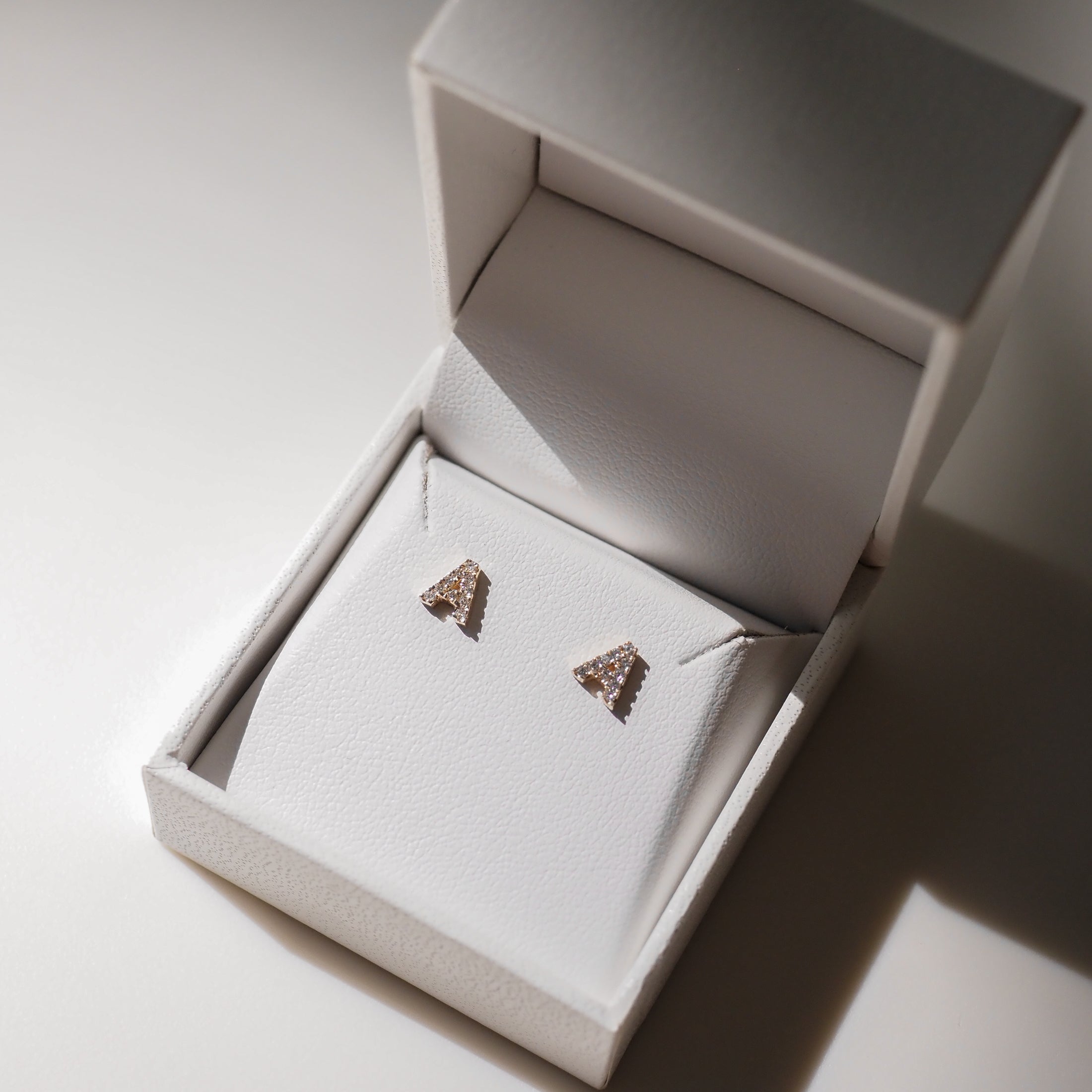 Triangle diamond stud earrings in a white jewellery box, illuminated softly, showcasing luxury and elegance.