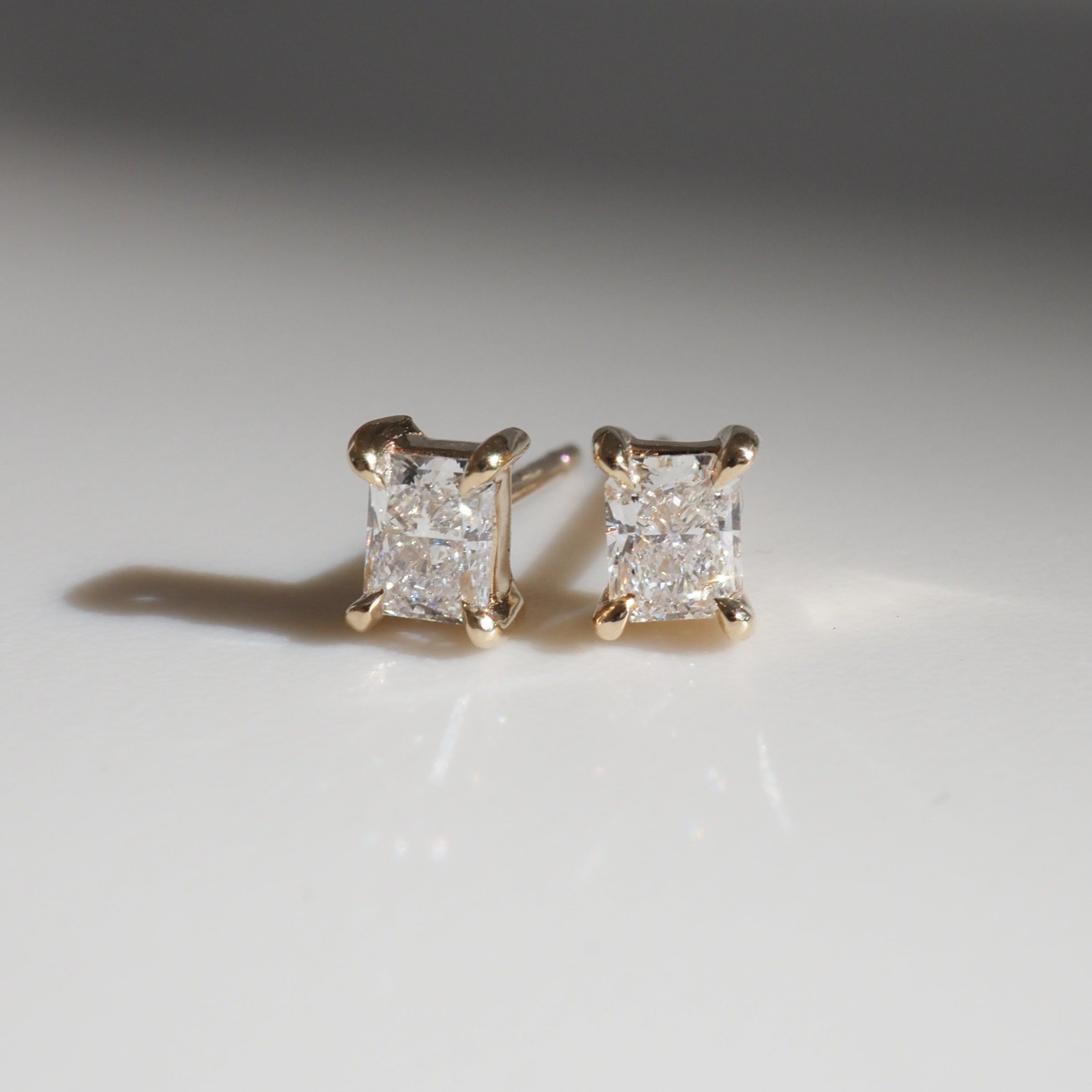 Pair of gold stud earrings with square-cut diamonds, elegantly displayed on a white surface. Perfect for luxury jewellery collectors.