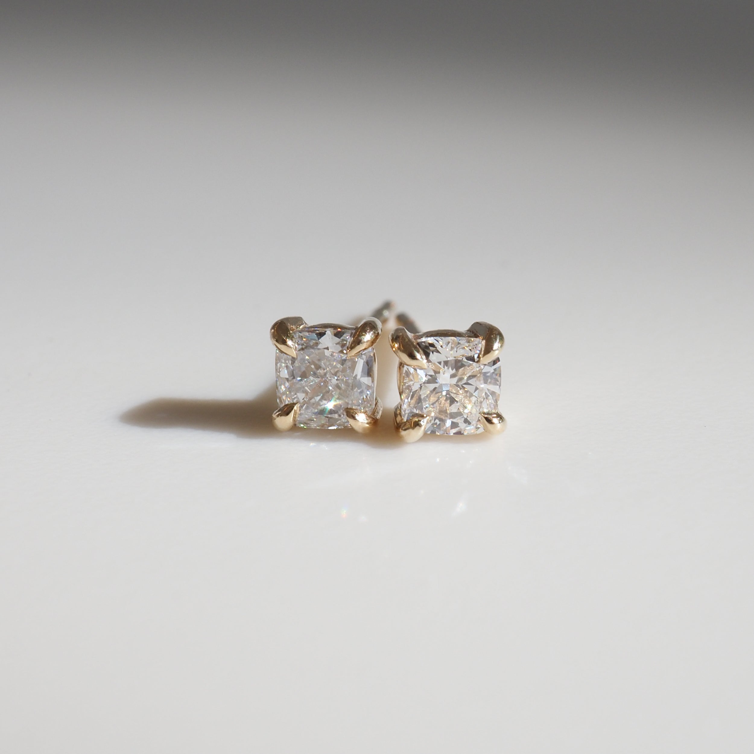 Two square-cut diamond stud earrings in elegant four-prong settings on a light background, showcasing luxury jewellery design.