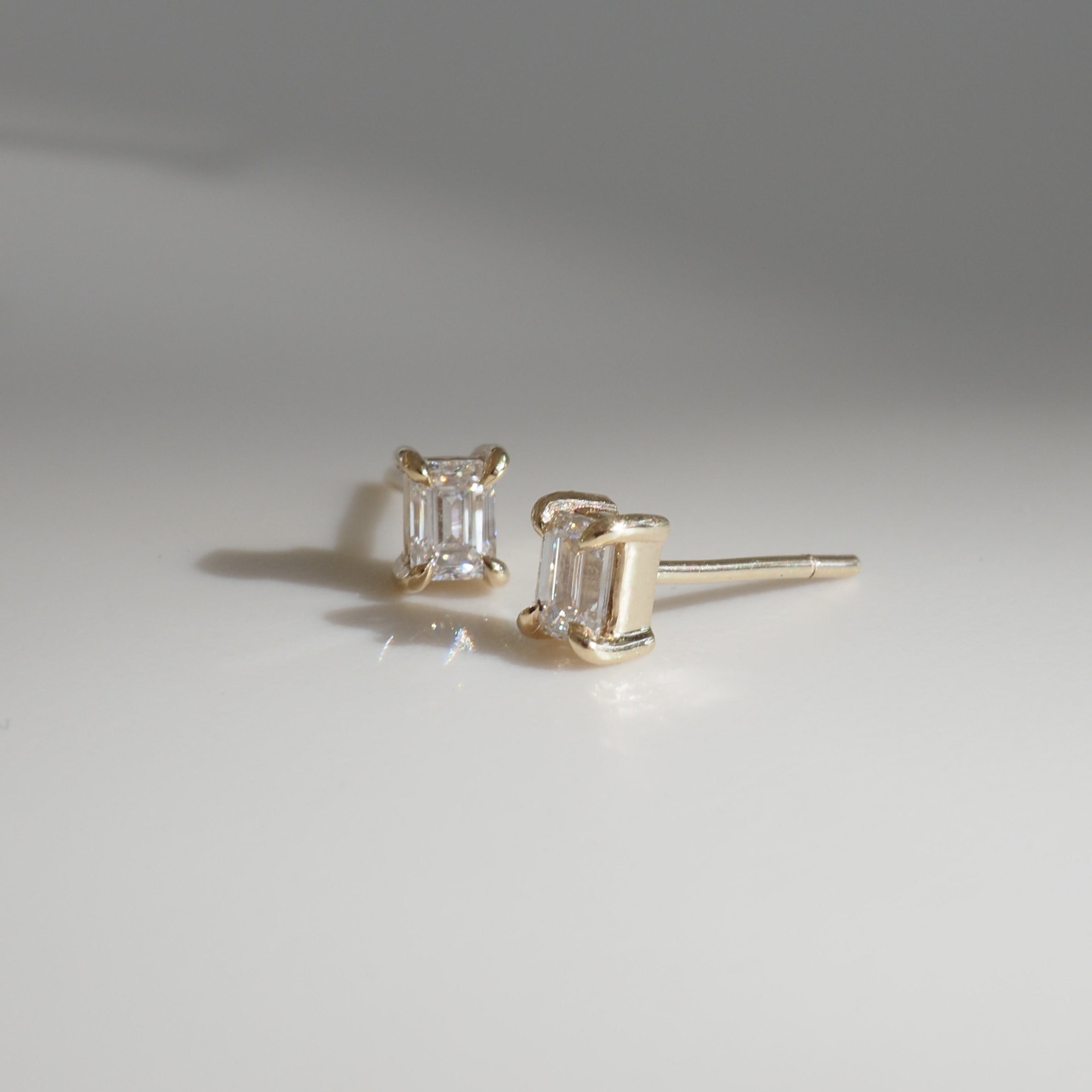 Elegant gold earrings featuring rectangular white diamonds, set on a reflective surface, signifying luxury jewellery craftsmanship.