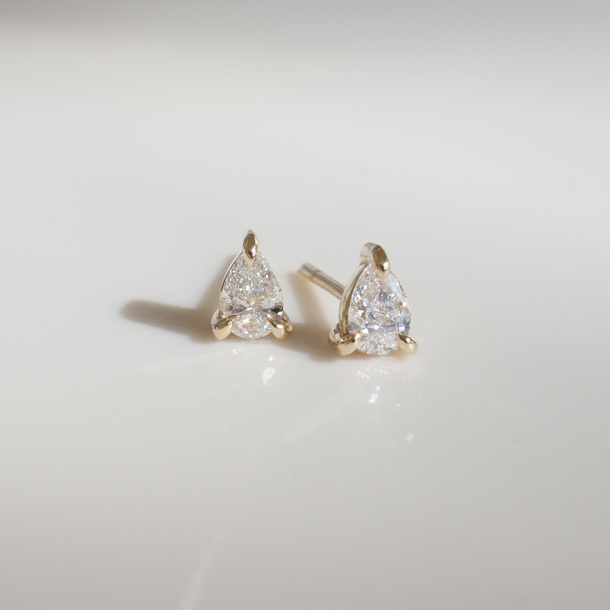 Elegant pear-shaped diamond stud earrings in a gold setting, placed on a sleek, reflective surface, capturing luxury jewellery essence.