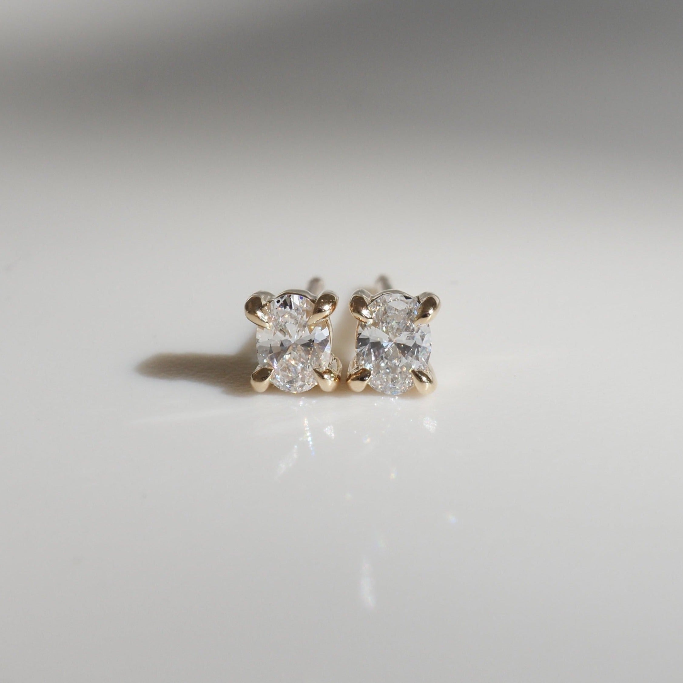 Elegant gold stud earrings with radiant cushion-cut diamonds on a reflective surface, showcasing luxury jewellery craftsmanship.