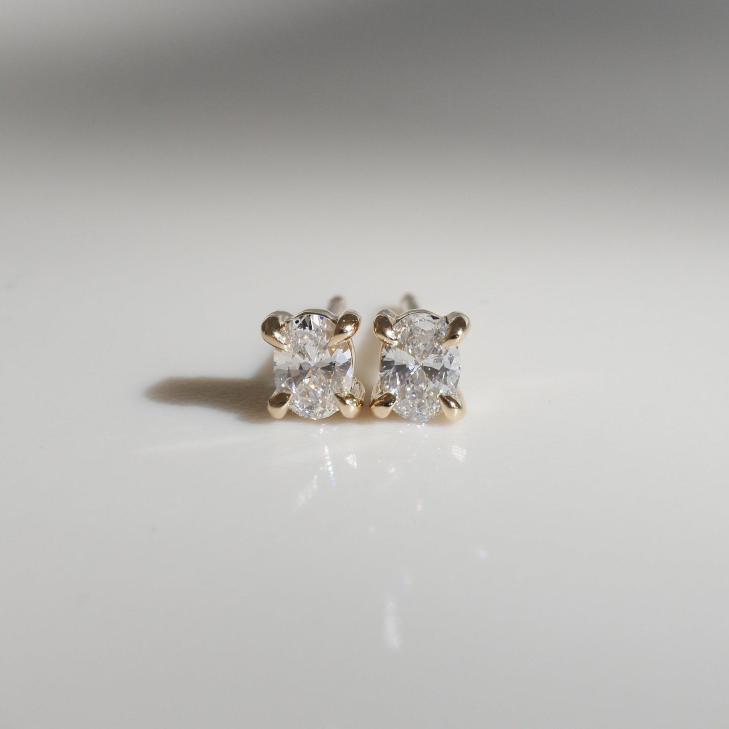 Gold diamond stud earrings on a reflective surface, showcasing luxury and elegance in fine jewellery craftsmanship.