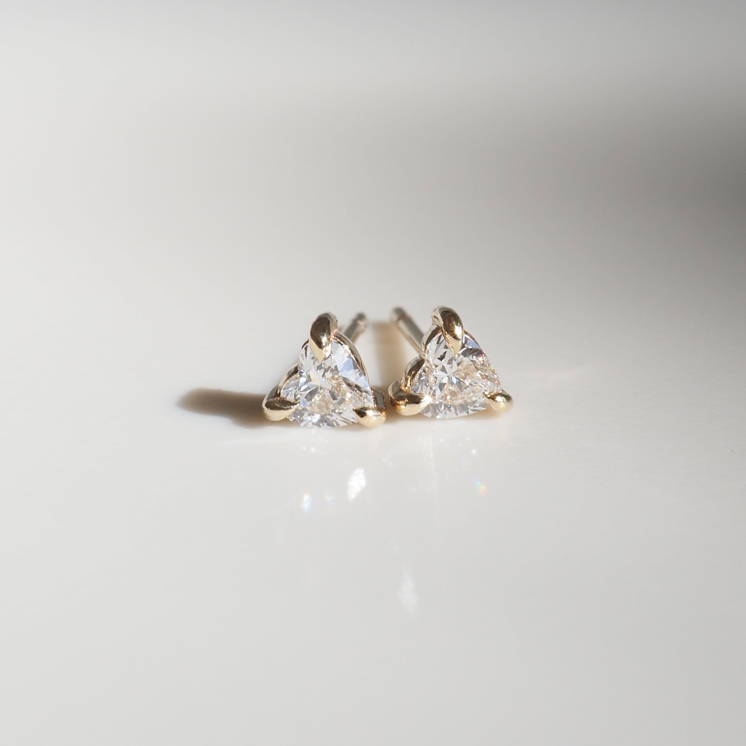 Trillion-cut diamond earrings set in gold, elegantly displayed on a smooth, well-lit surface, perfect for luxury jewellery lovers.