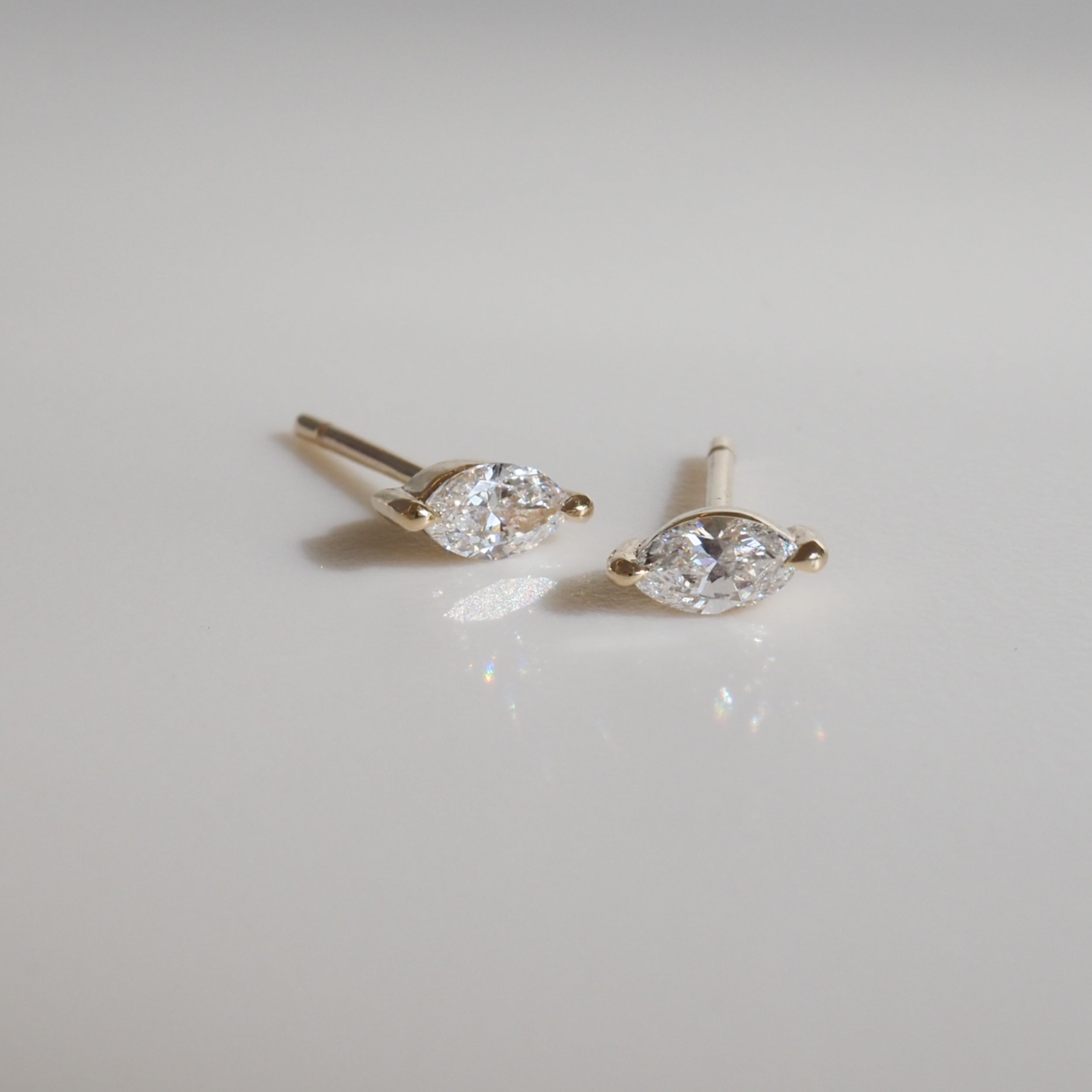 Gold marquise diamond earrings with delicate prong settings on a white background, reflecting light subtly. Luxurious fine jewellery.