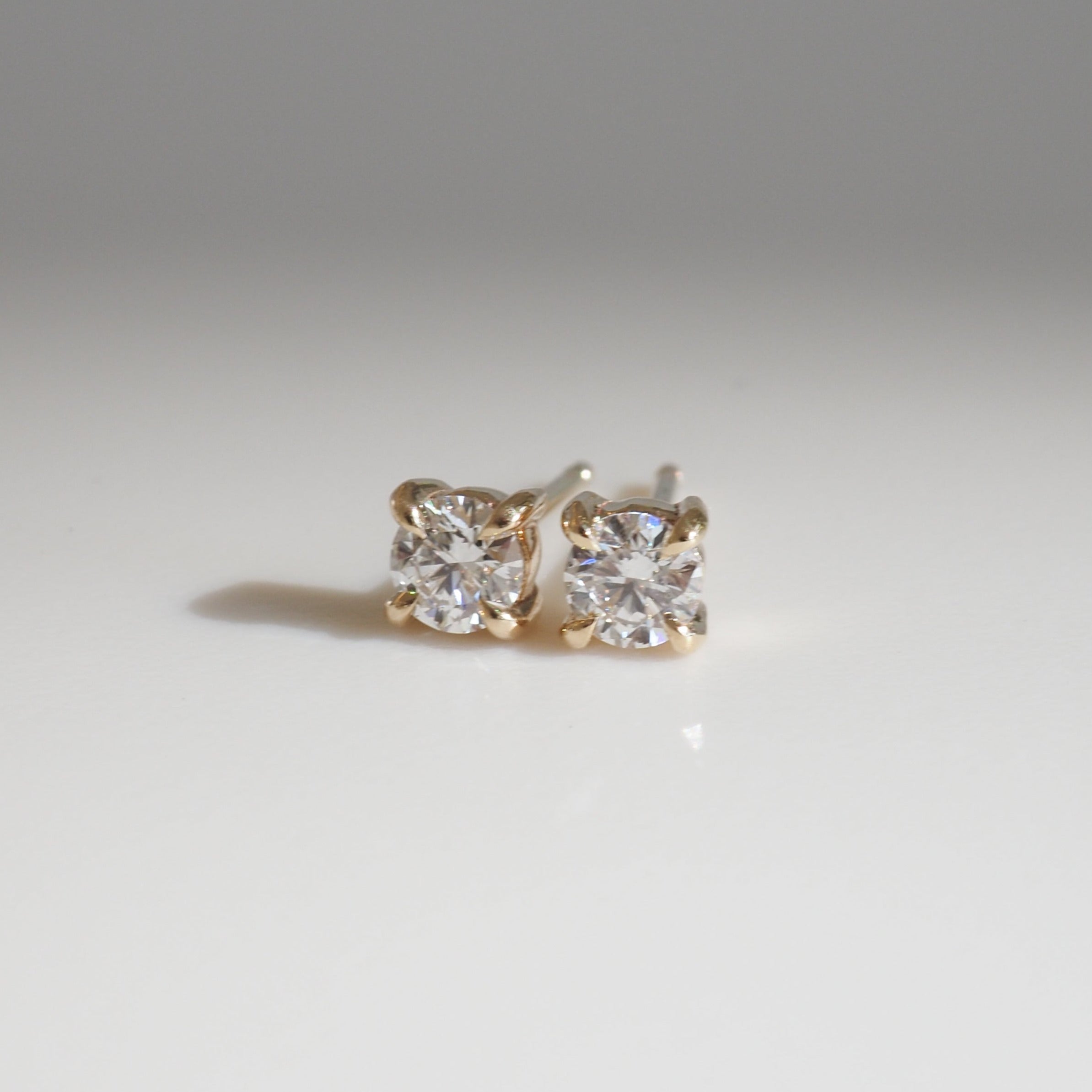 Gold diamond stud earrings on a smooth, reflective surface. Perfect for high-end jewellery enthusiasts.