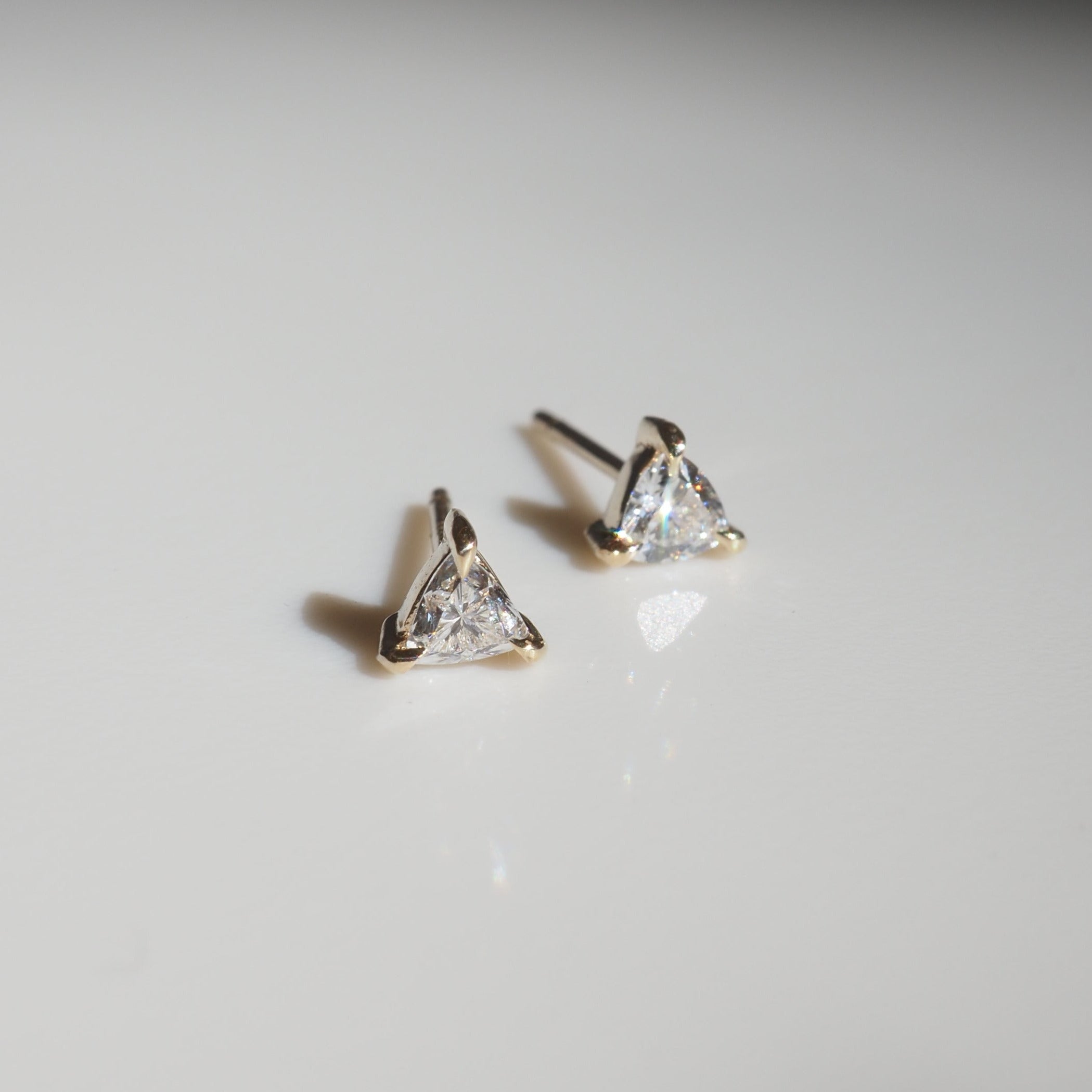 Triangular diamond earrings with a gold prong setting on a white surface, elegantly designed for luxury jewellery enthusiasts.