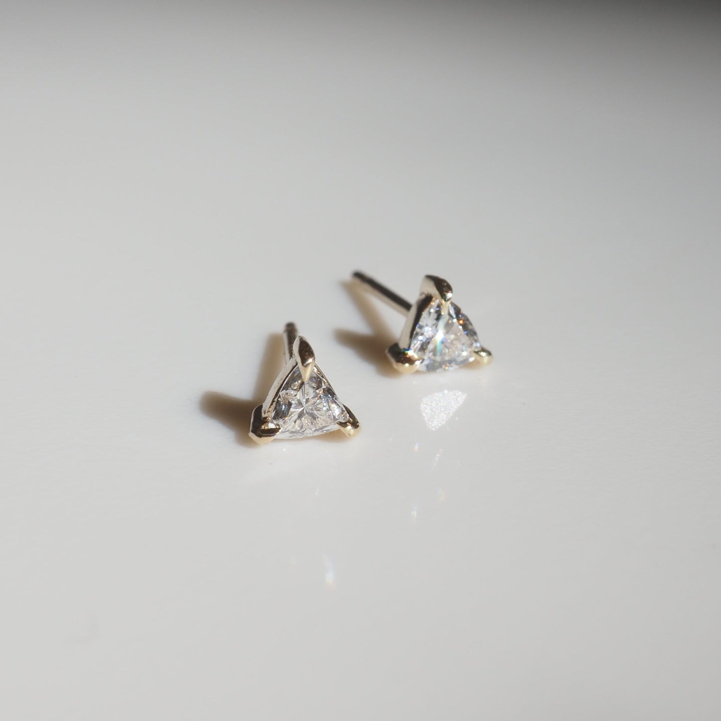 Triangular diamond stud earrings set in gold, placed on a sleek white surface, showcasing luxury jewellery elegance.