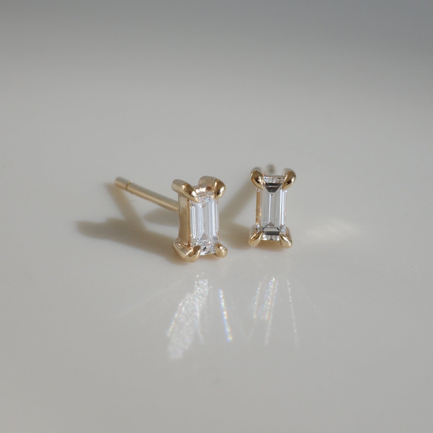Elegant emerald-cut diamond stud earrings in gold setting on a smooth, reflective surface. Ideal luxury jewellery piece.