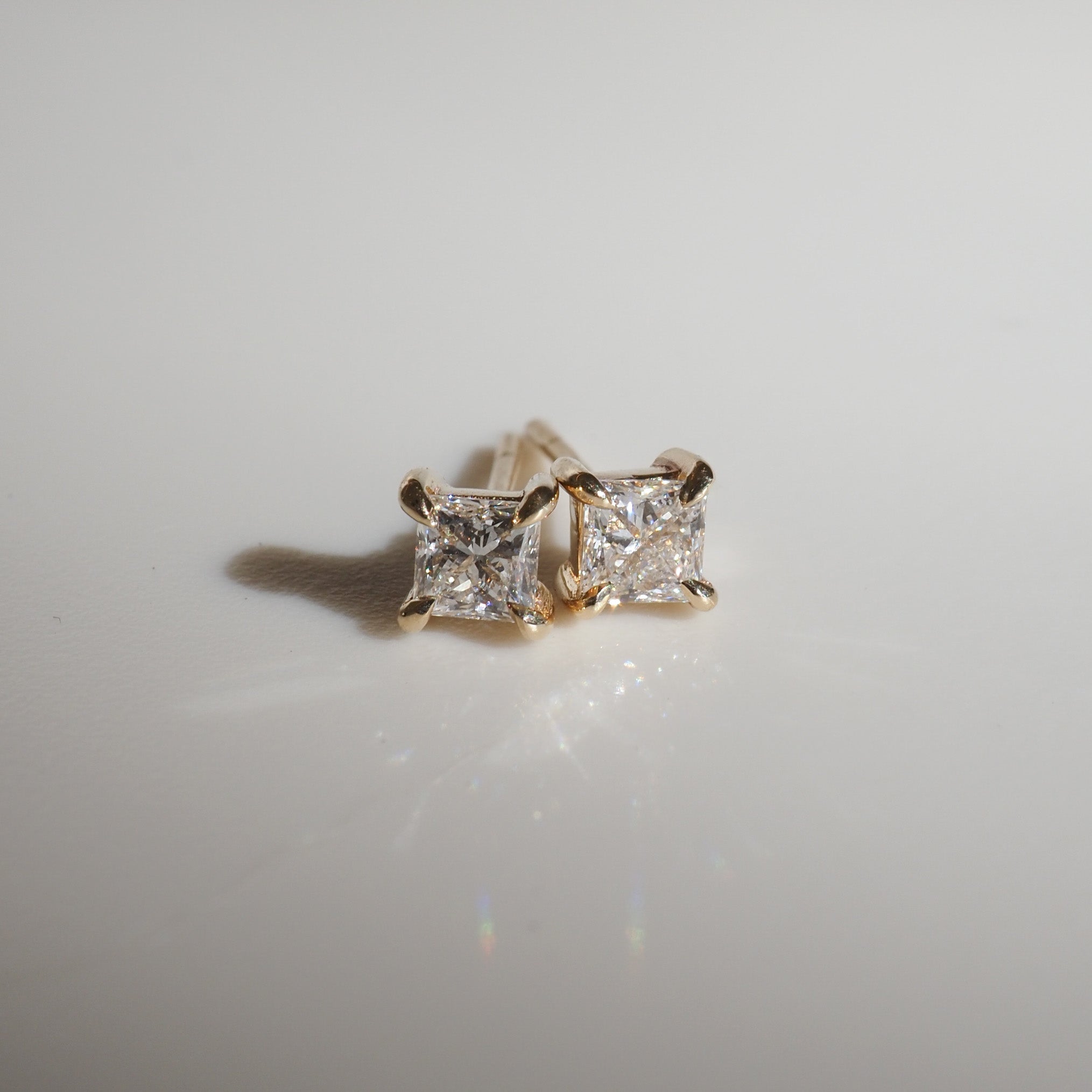 Gold stud earrings with square-cut diamonds on a smooth surface, reflecting light. Elegant and luxurious jewellery piece.