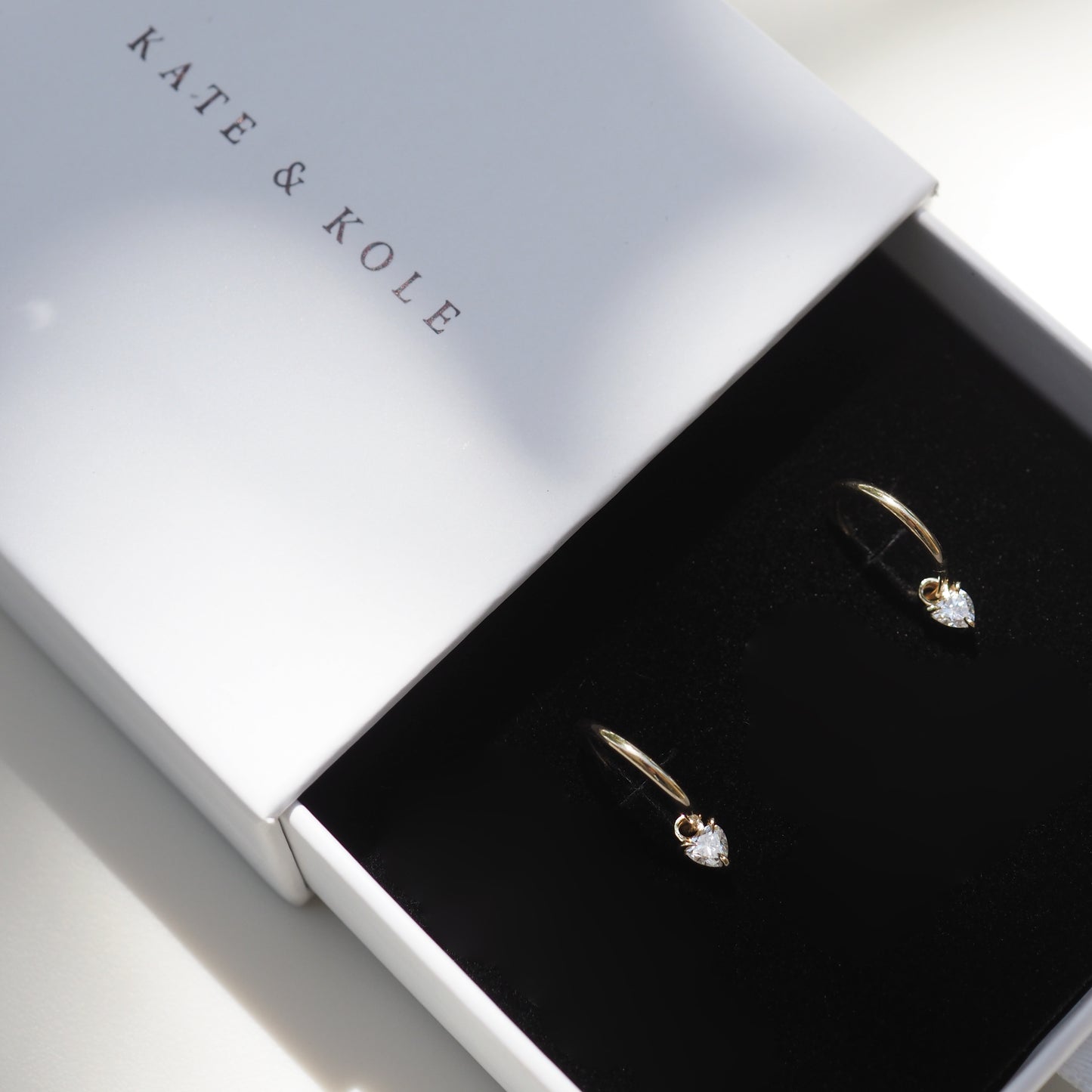 Gift box with two gold earrings featuring teardrop-shaped gems, branded "Kate & Kole", on a white background. Luxurious jewellery packaging.