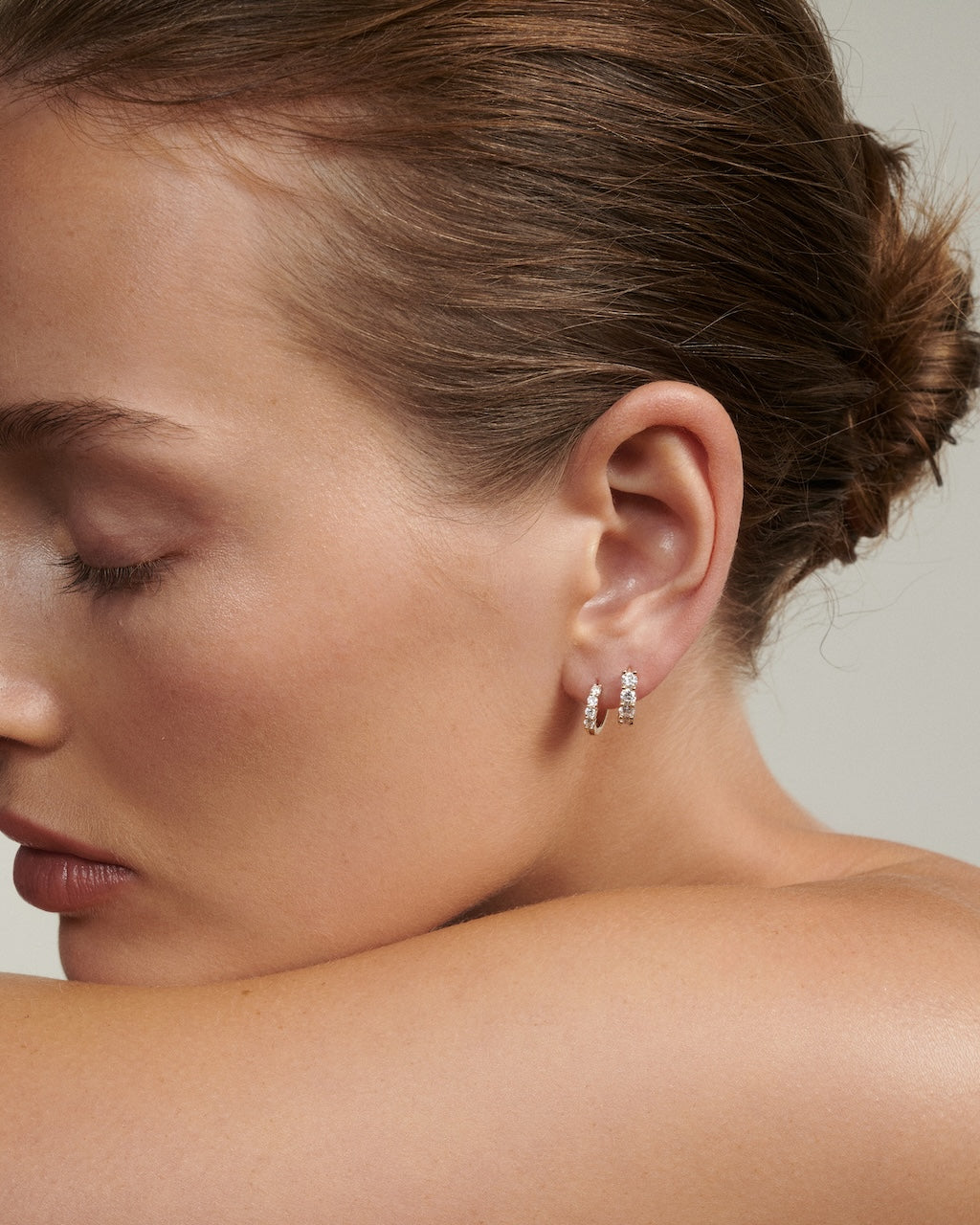 Close-up of a woman wearing a diamond huggie hoop earring on a neutral background