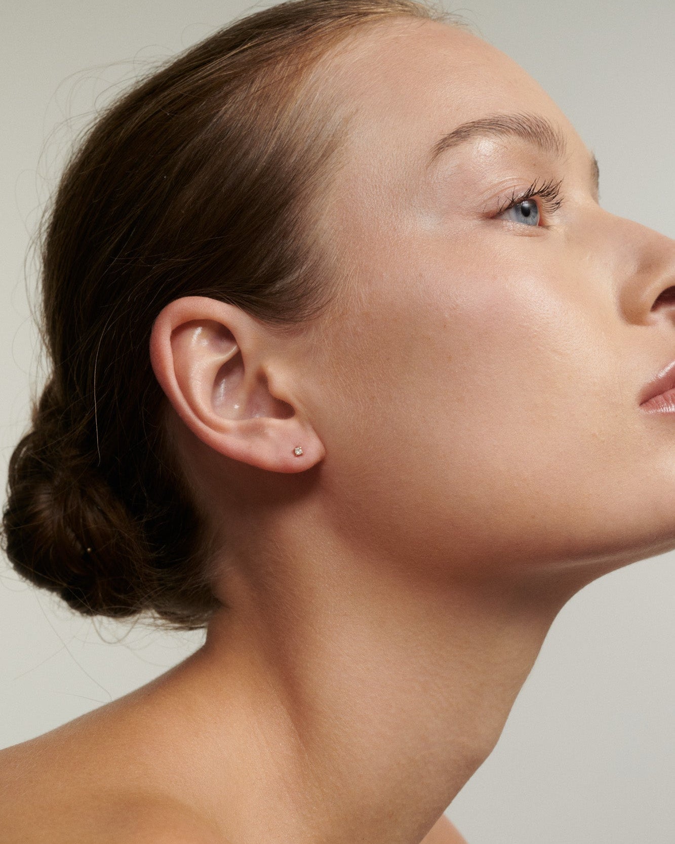 Close-up of a woman's ear with a small earring against a neutral background
