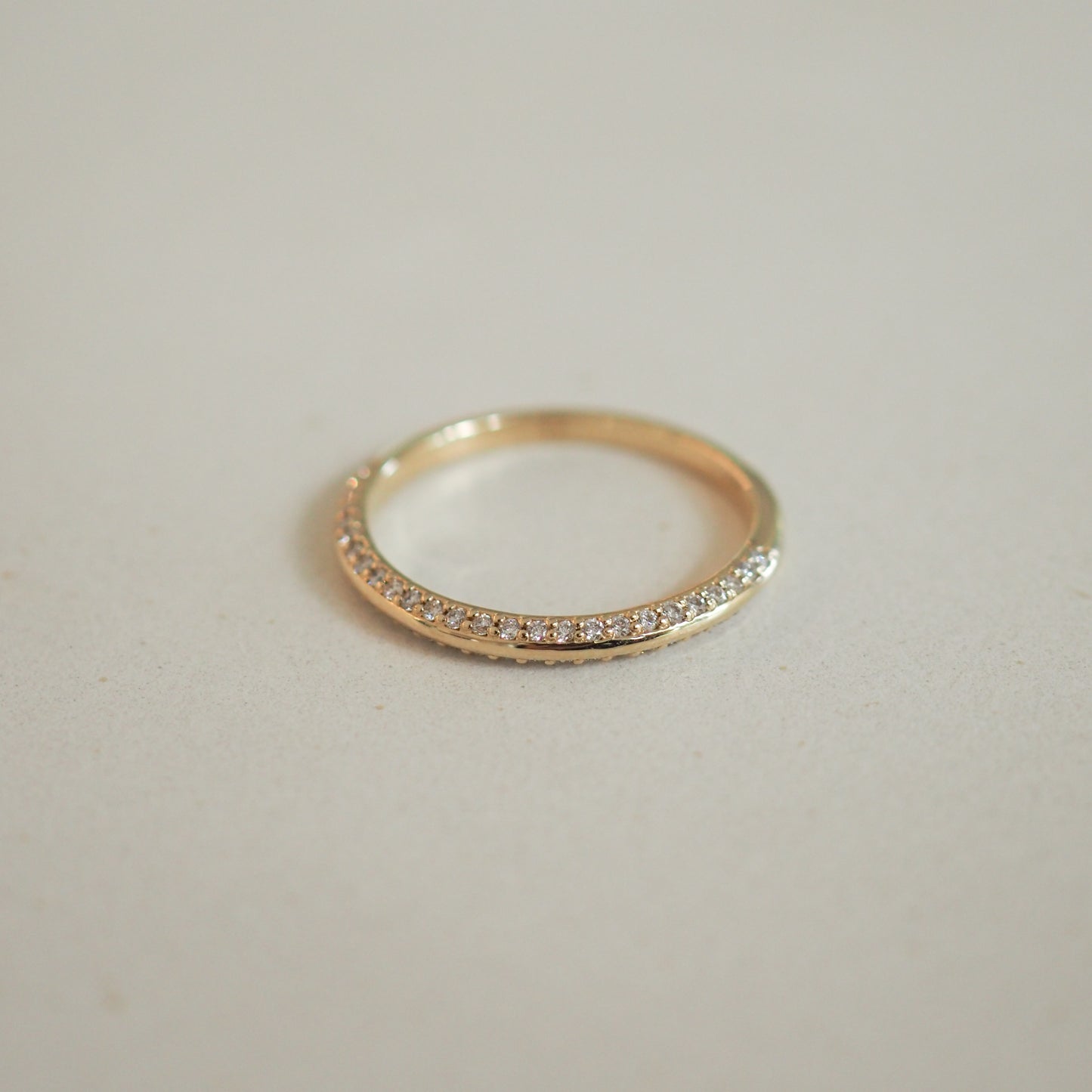 Elegant gold ring with a half-eternity band of sparkling diamonds, showcasing luxury jewellery craftsmanship on a neutral background.