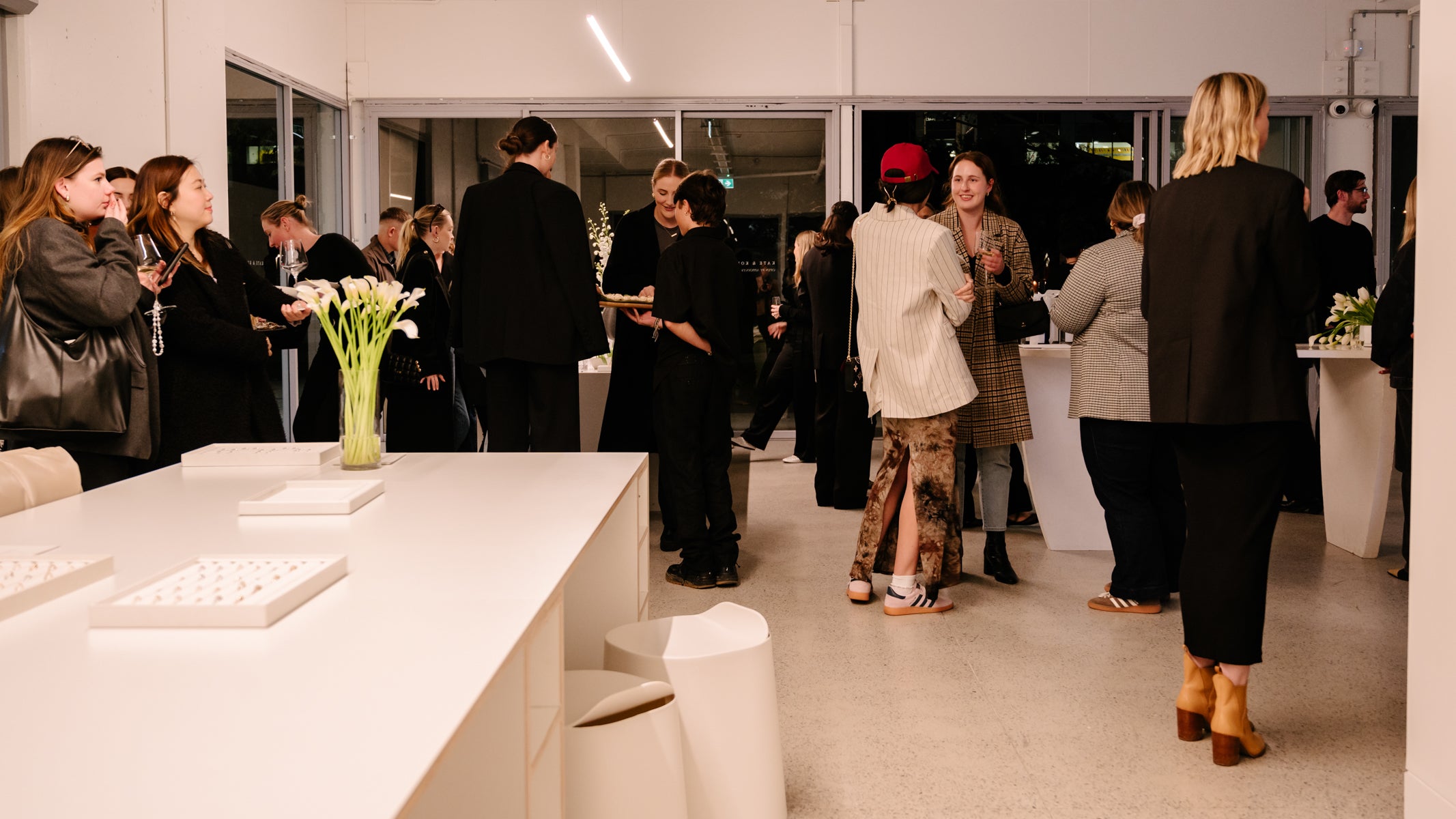 Elegant jewellery event in a chic showroom; attendees mingle around displays and white decor, exuding a luxury atmosphere.