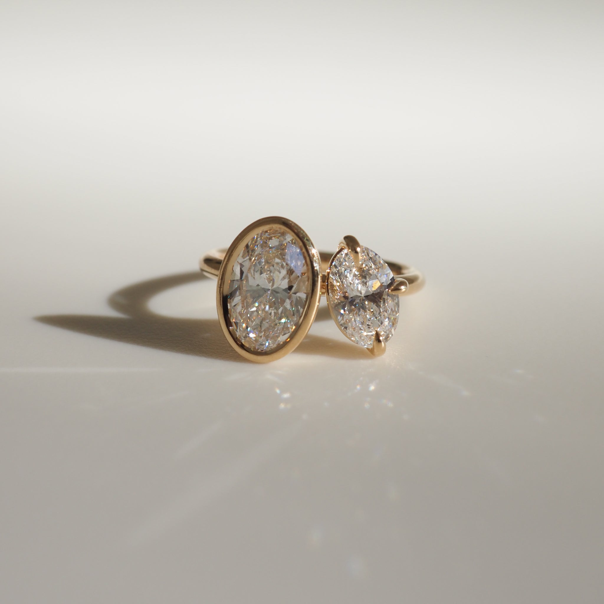 Gold ring with an oval diamond and two heart-shaped diamonds, elegantly displayed on a soft, light background; luxury jewellery design.