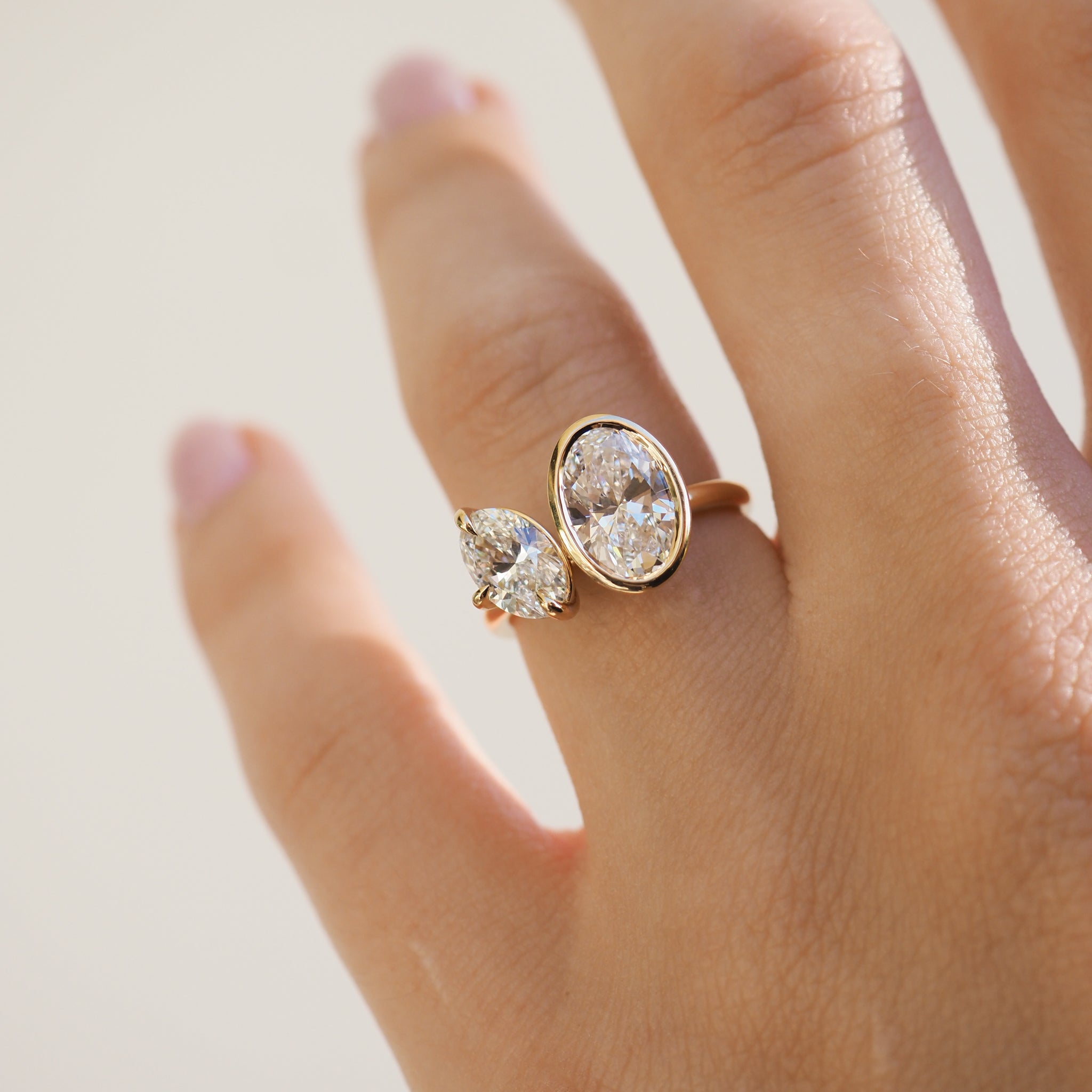 Gold double-band ring with pear and oval-cut diamonds on a hand. Sunlit luxury jewellery, showcasing elegance and premium design.