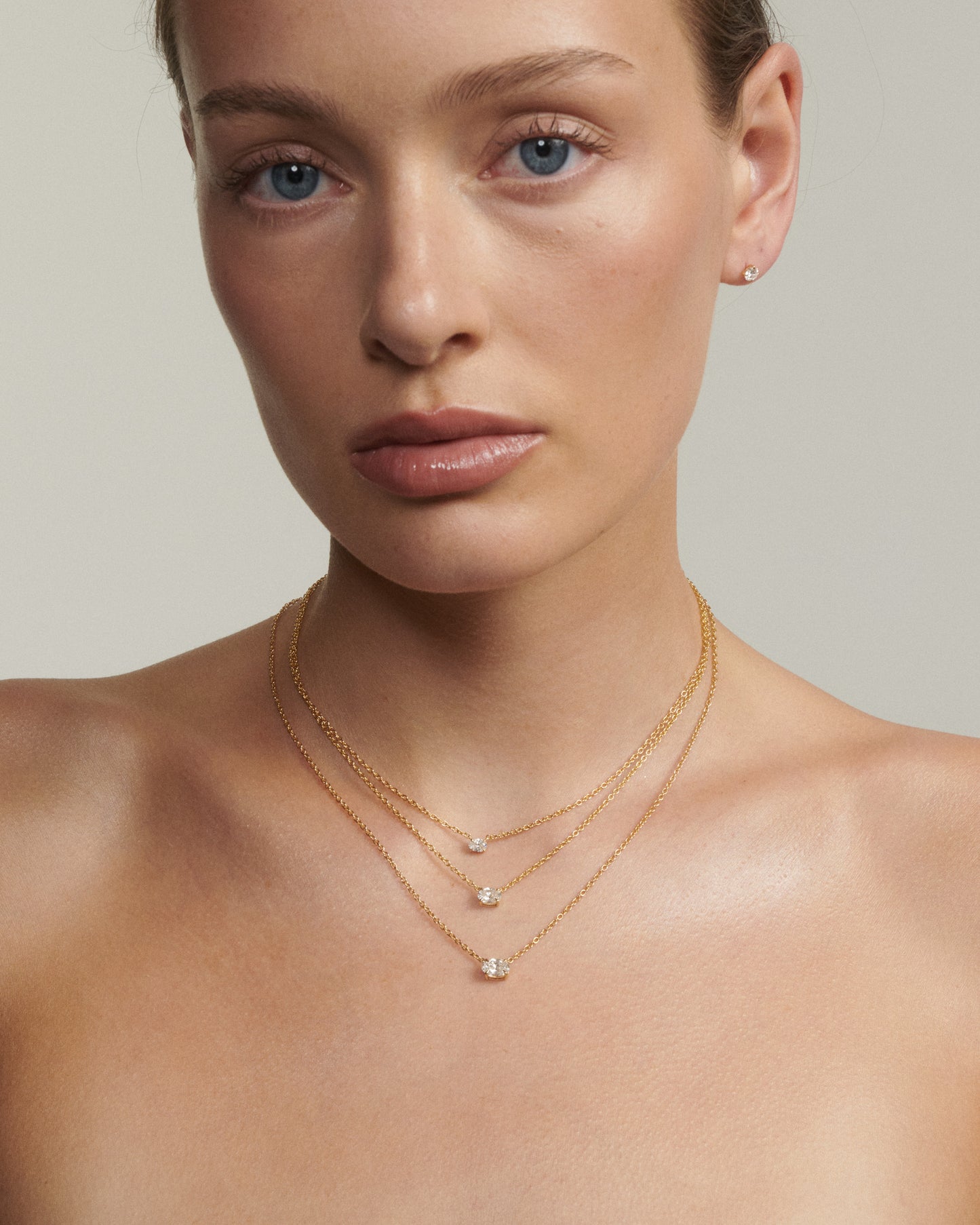 Woman wearing a delicate gold necklace with small pendants against a neutral background