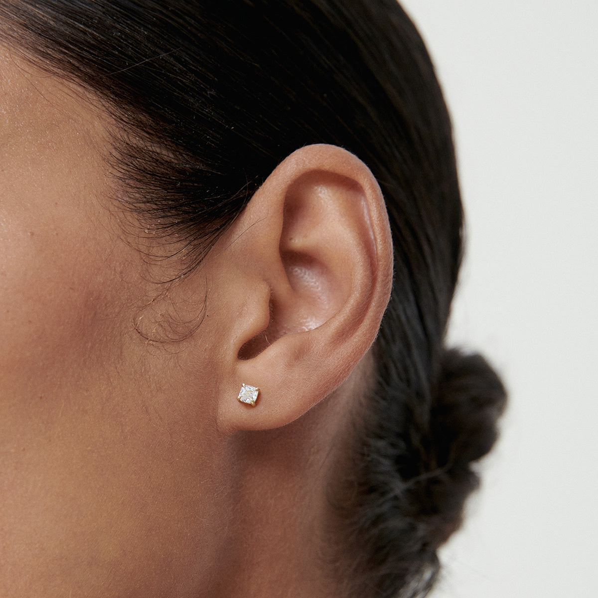 Close-up of an ear adorned with a small, elegant diamond stud earring, highlighting luxury jewellery against a simple background.