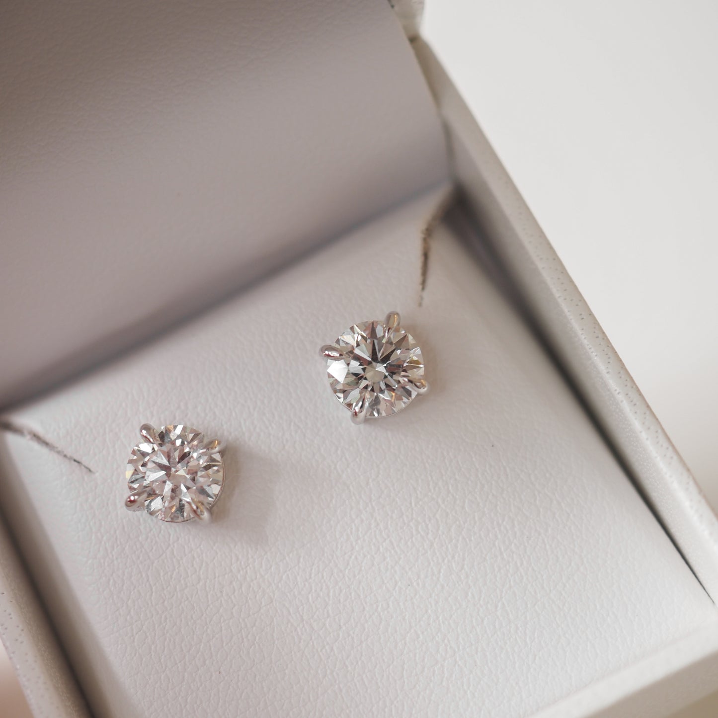 Diamond stud earrings in an elegant white jewellery box, showcasing luxury and sophistication.