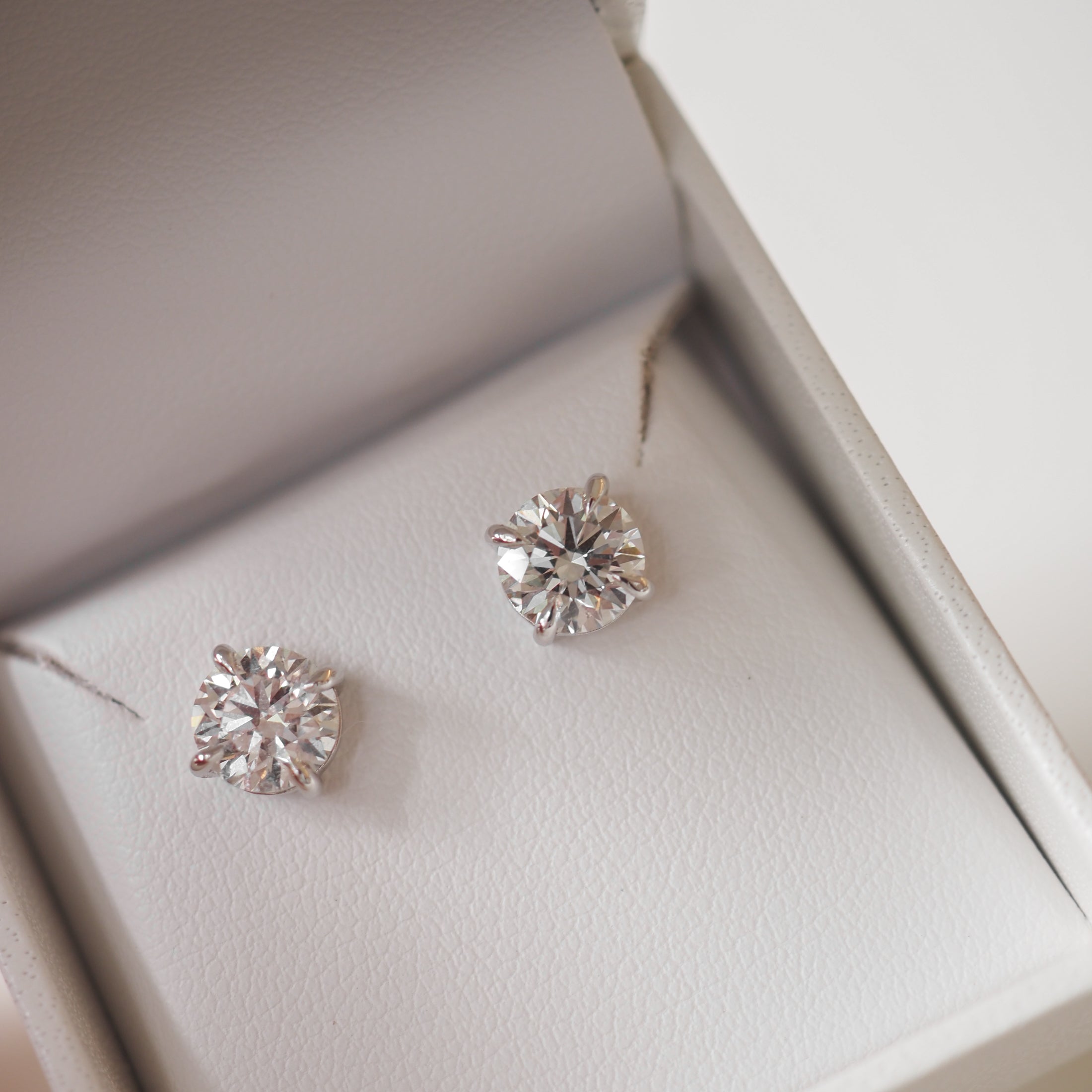 Diamond stud earrings in an elegant white jewellery box, showcasing luxury and sophistication.