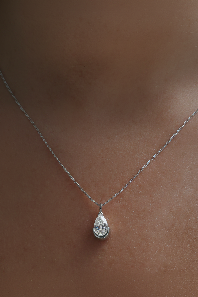 Gold necklace with a pear-shaped diamond pendant against skin, showcasing luxury jewellery.