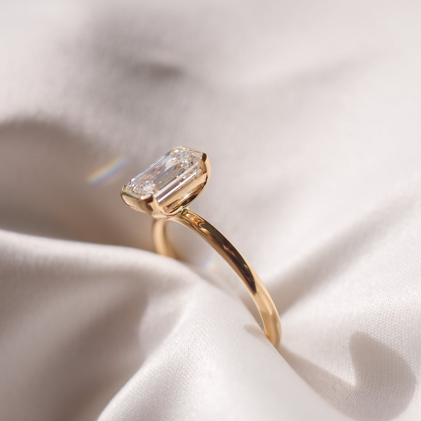 Emerald-cut diamond ring on a smooth, white fabric. The gold band highlights the gemstone's clarity and elegance. Perfect luxury jewellery piece.