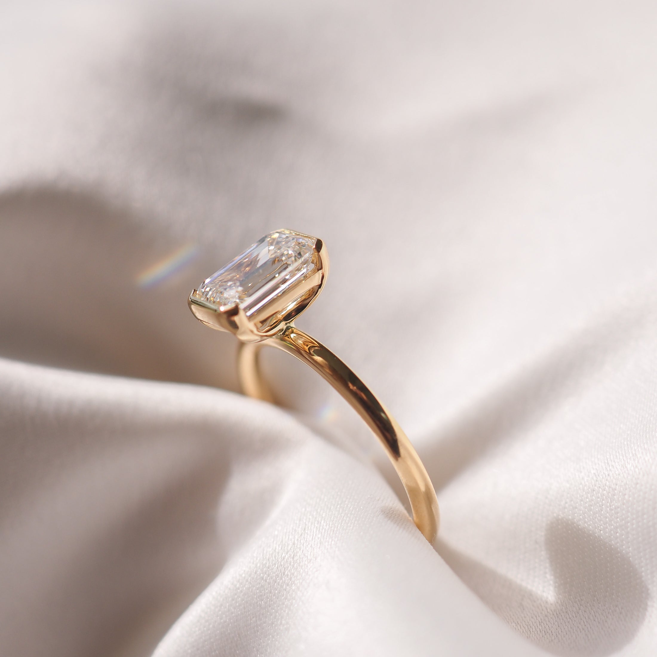 Emerald-cut diamond ring on a smooth, white fabric. The gold band highlights the gemstone's clarity and elegance. Perfect luxury jewellery piece.