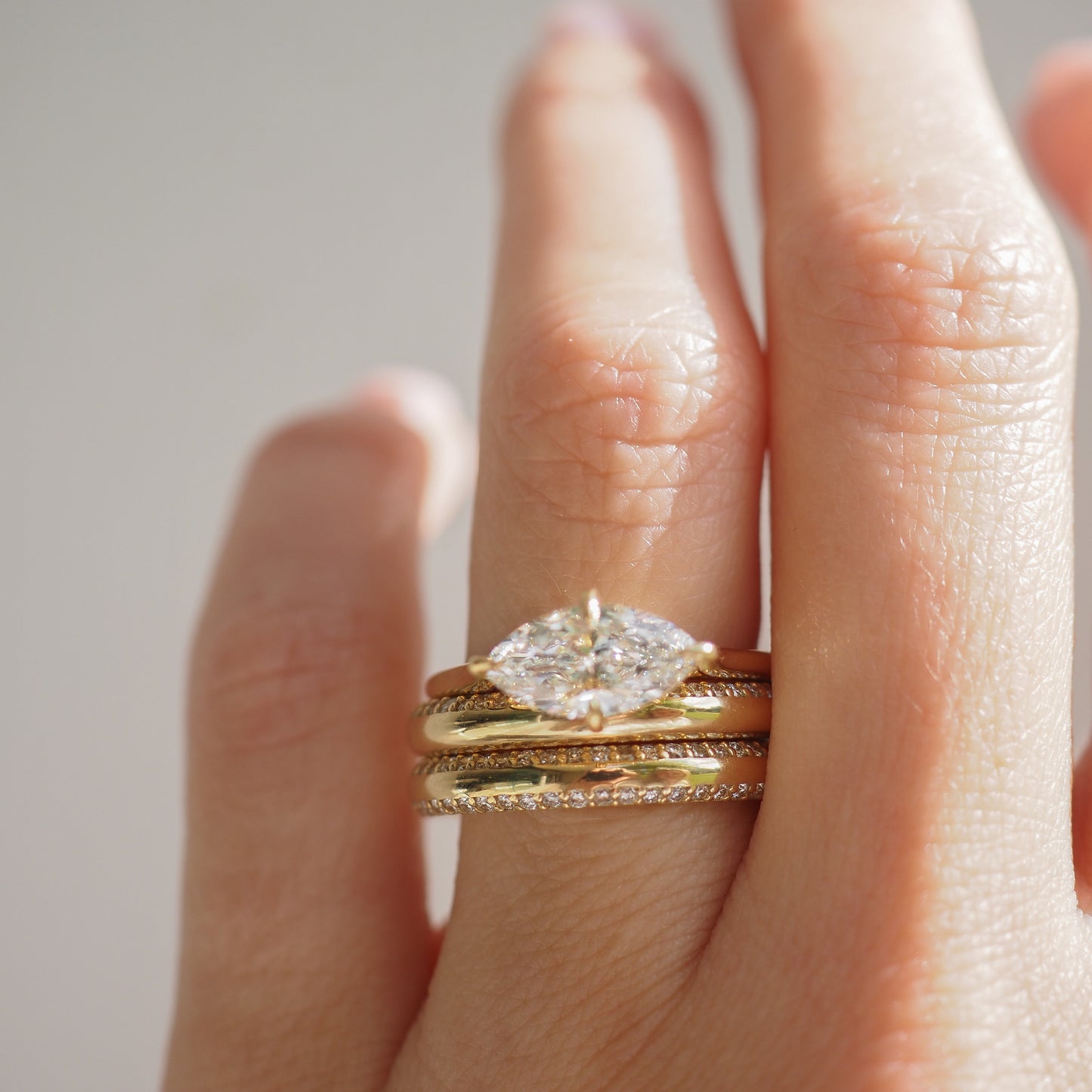 Close-up of a hand wearing a marquise diamond ring stacked with gold and diamond-studded bands, showcasing luxury jewellery in soft natural light.