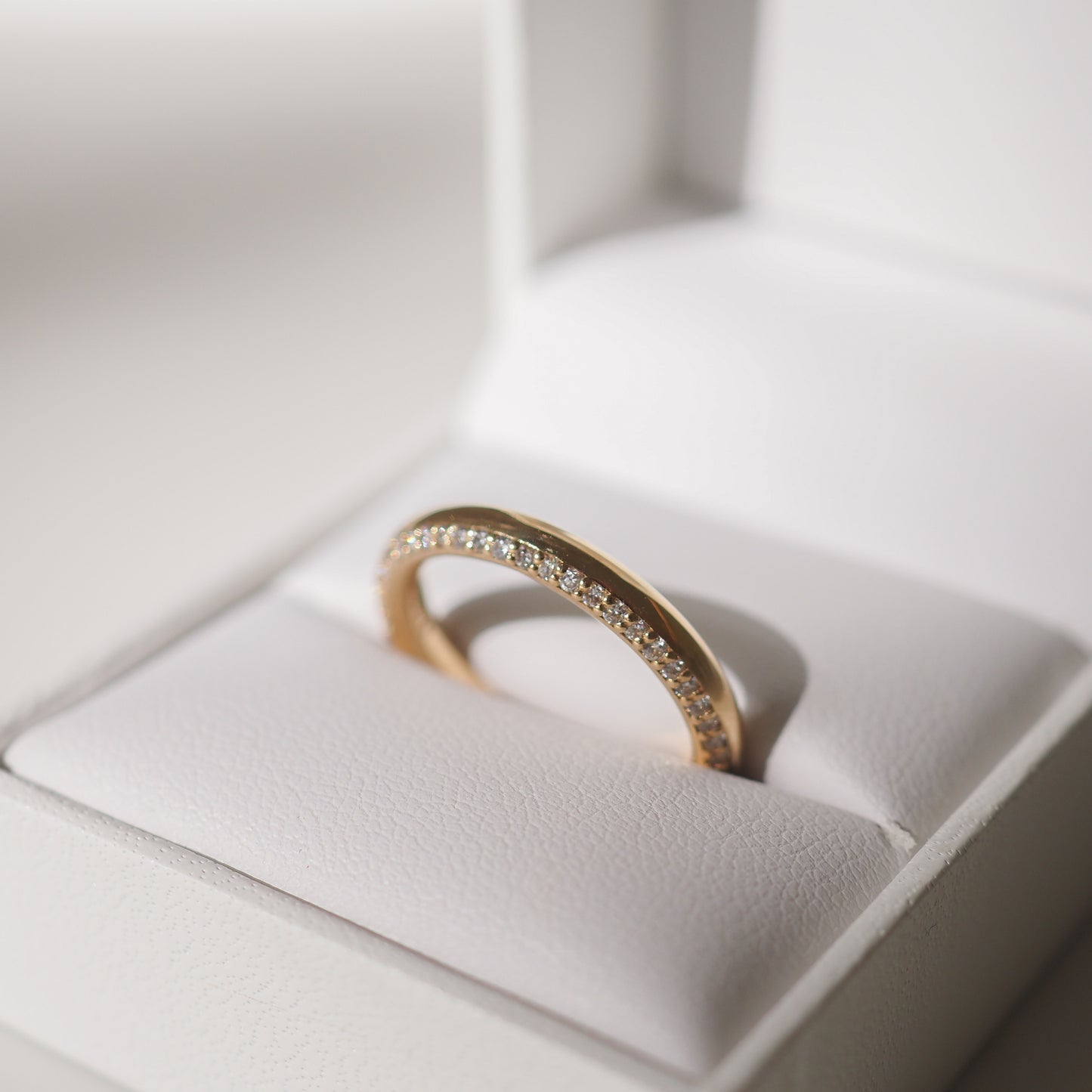 Gold diamond band in a white jewellery box, elegantly displayed in soft lighting, highlighting its luxurious design and sparkling stones.