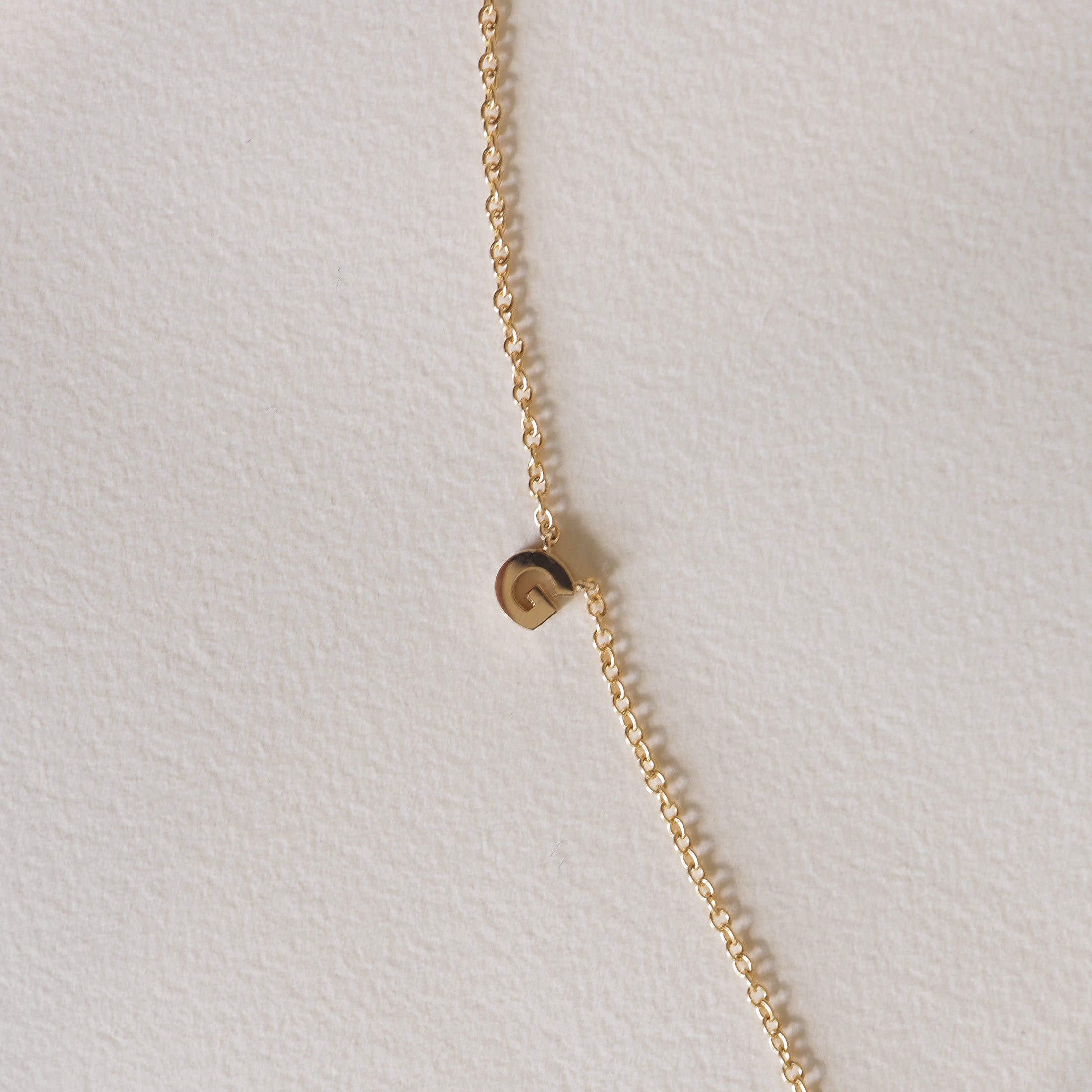 Elegant gold chain with a small pendant featuring the letter 'G' on a neutral background; minimalist luxury jewellery design.