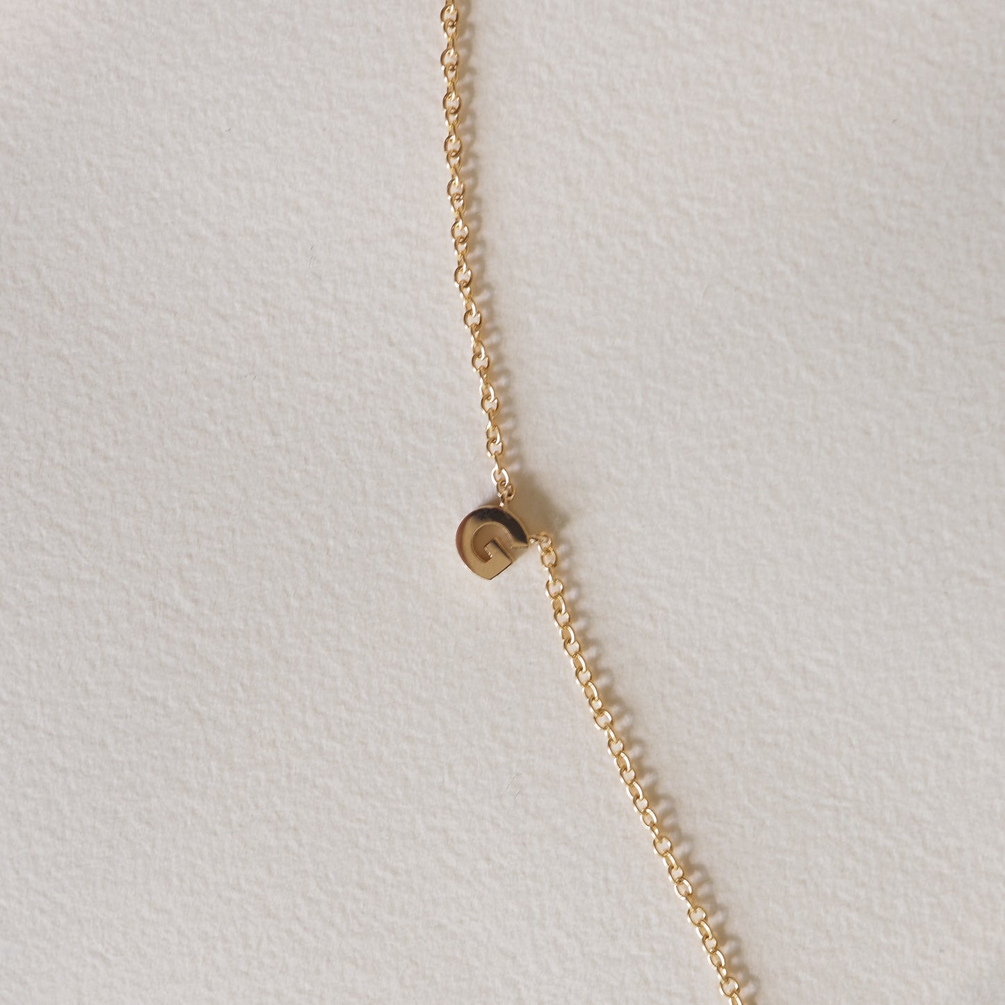 Delicate gold chain necklace with a small, engraved disc pendant against a light background. Luxury jewellery piece.