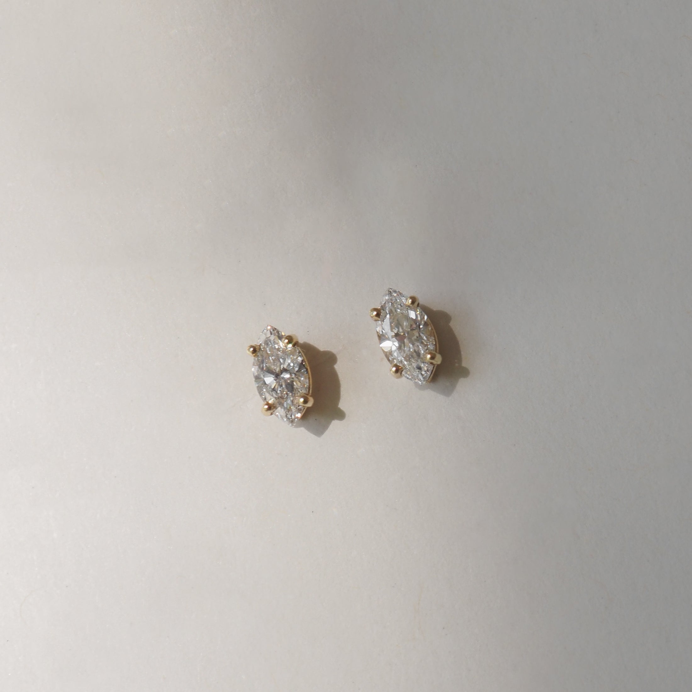 Marquise-cut diamond stud earrings with gold prongs, elegantly displayed on a soft grey background. Perfect for luxury jewellery lovers.