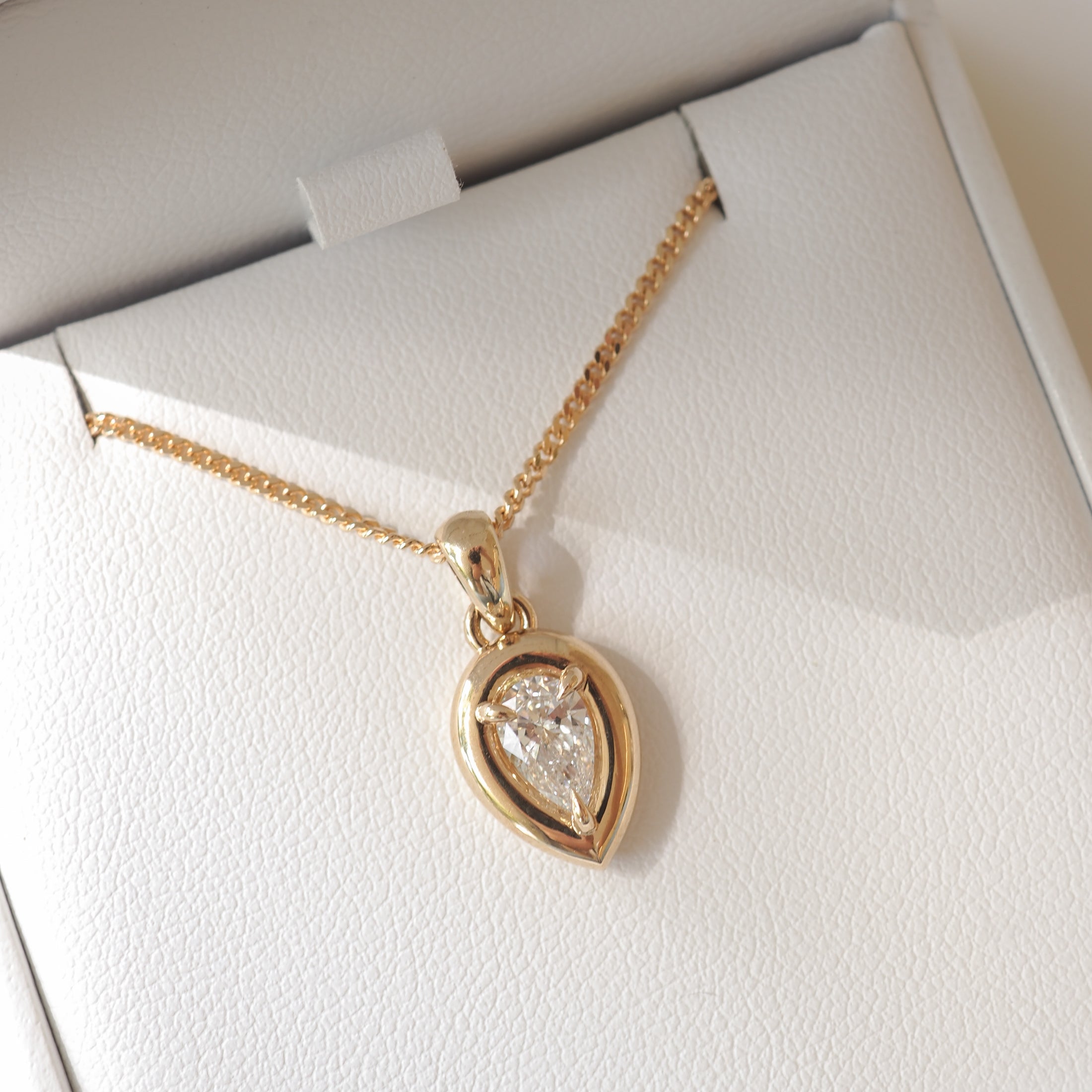 Gold necklace with a pear-shaped diamond pendant in a white jewellery box; luxury jewellery design.