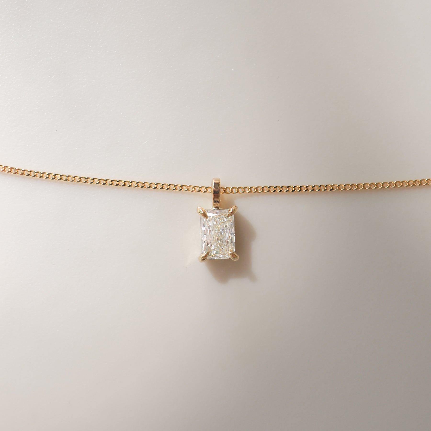 Gold chain necklace featuring a radiant-cut diamond pendant against a neutral background; luxury jewellery.