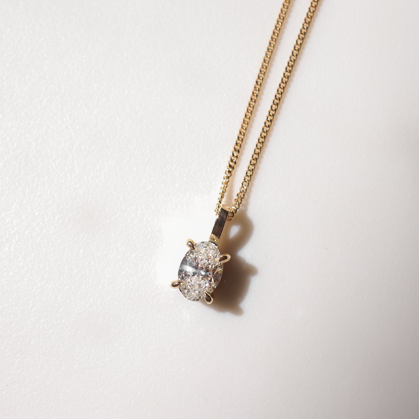 Gold chain necklace with an oval diamond pendant on a soft white background, highlighting luxury jewellery elegance.