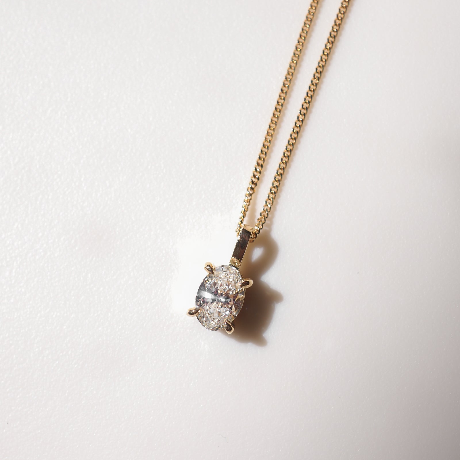 Gold chain necklace with an oval diamond pendant on a soft white background, highlighting luxury jewellery elegance.