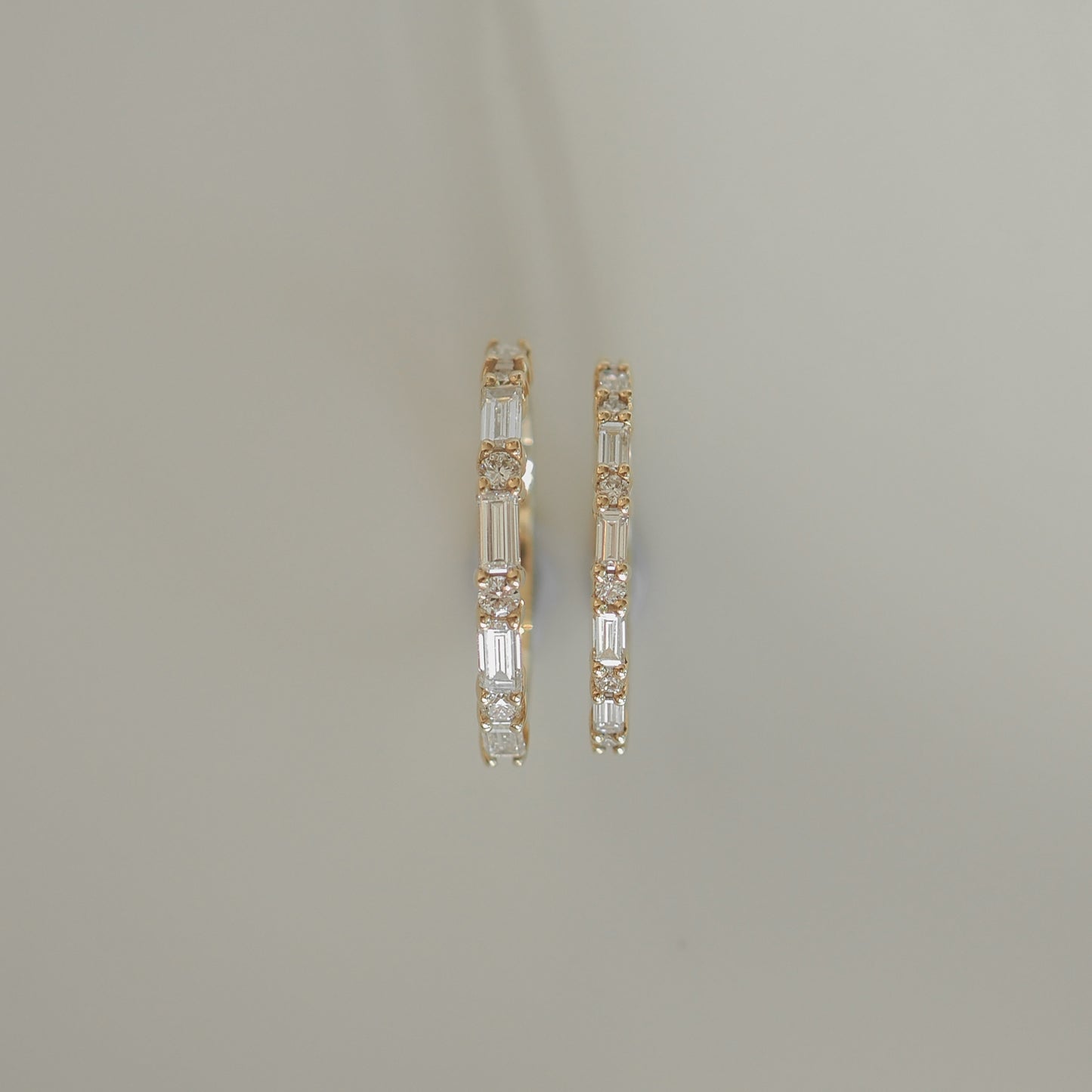 Gold hoop earrings with alternating baguette and round diamonds on a light grey background. Luxurious jewellery design.