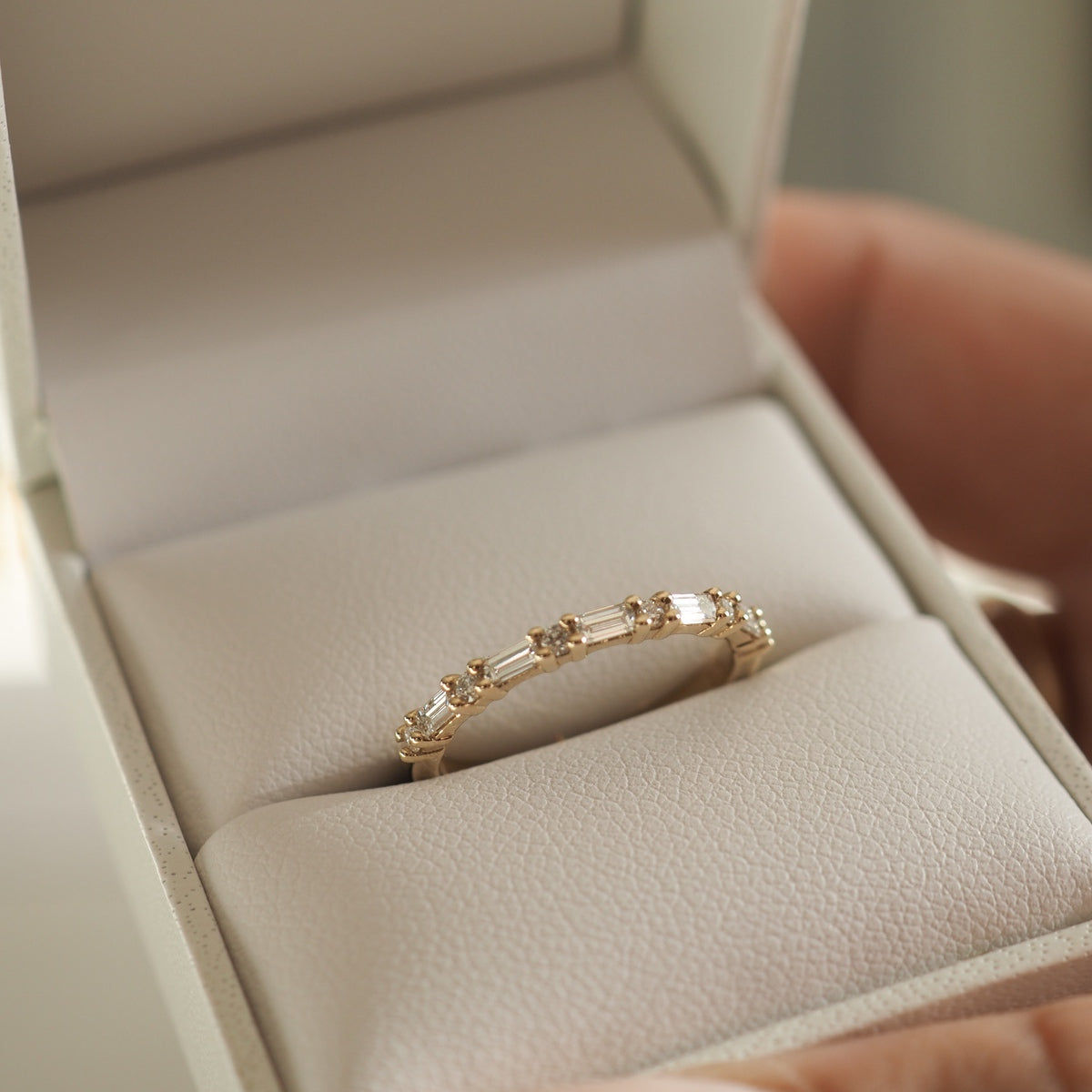 Gold band ring with rectangular gemstones in an open box, held by a hand. Perfect for a luxury jewellery gift idea.