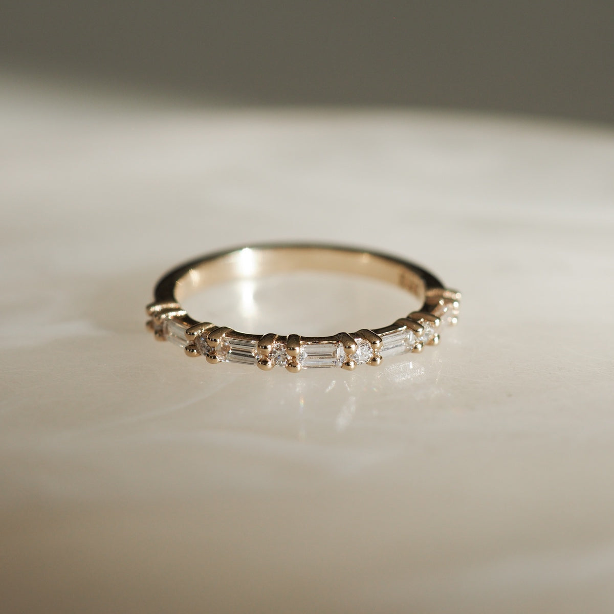 Gold band with baguette-cut diamonds elegantly set, lying on a marble surface, capturing a luxury jewellery aesthetic.