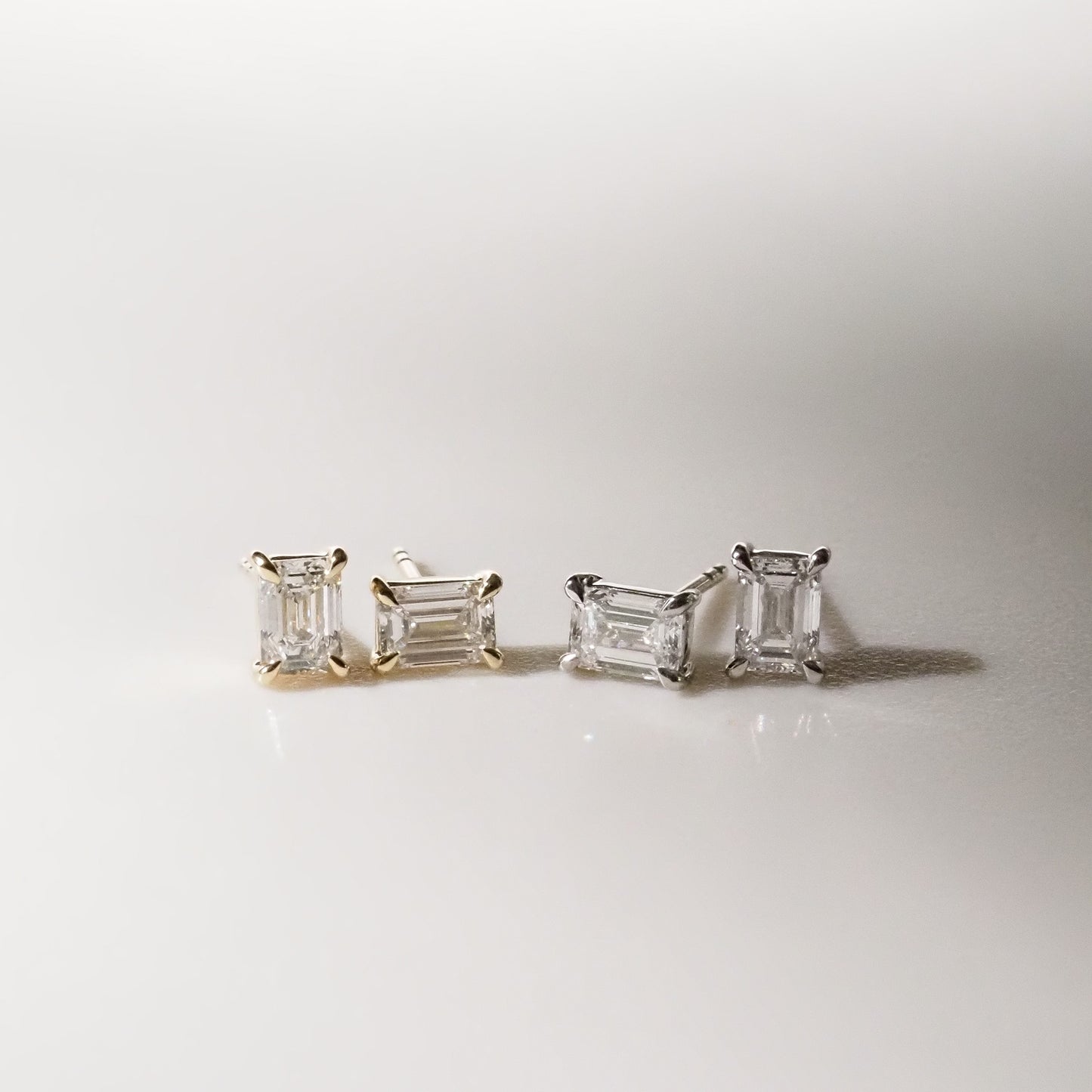 Two pairs of emerald diamond earrings on a light gray background