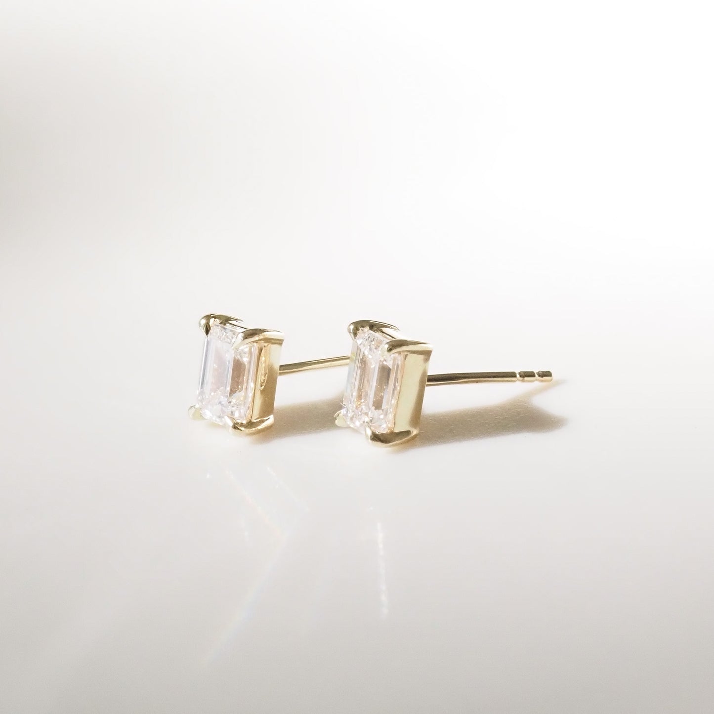 Gold stud earrings with clear gemstones on a light gray background