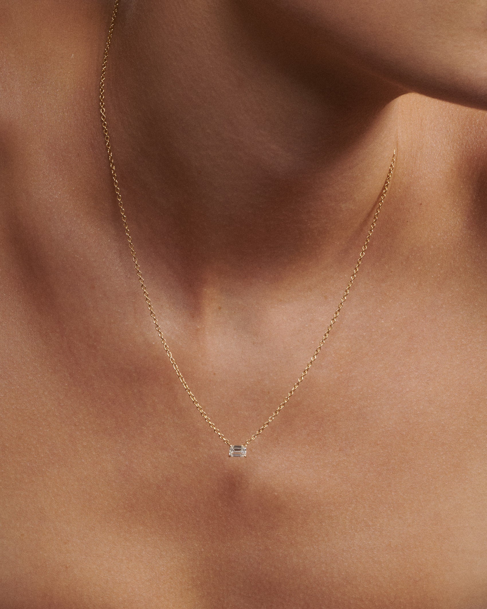 Gold necklace with a small pendant on a person's neck [text overlay: Andrea wears the 0.5ct Necklace]