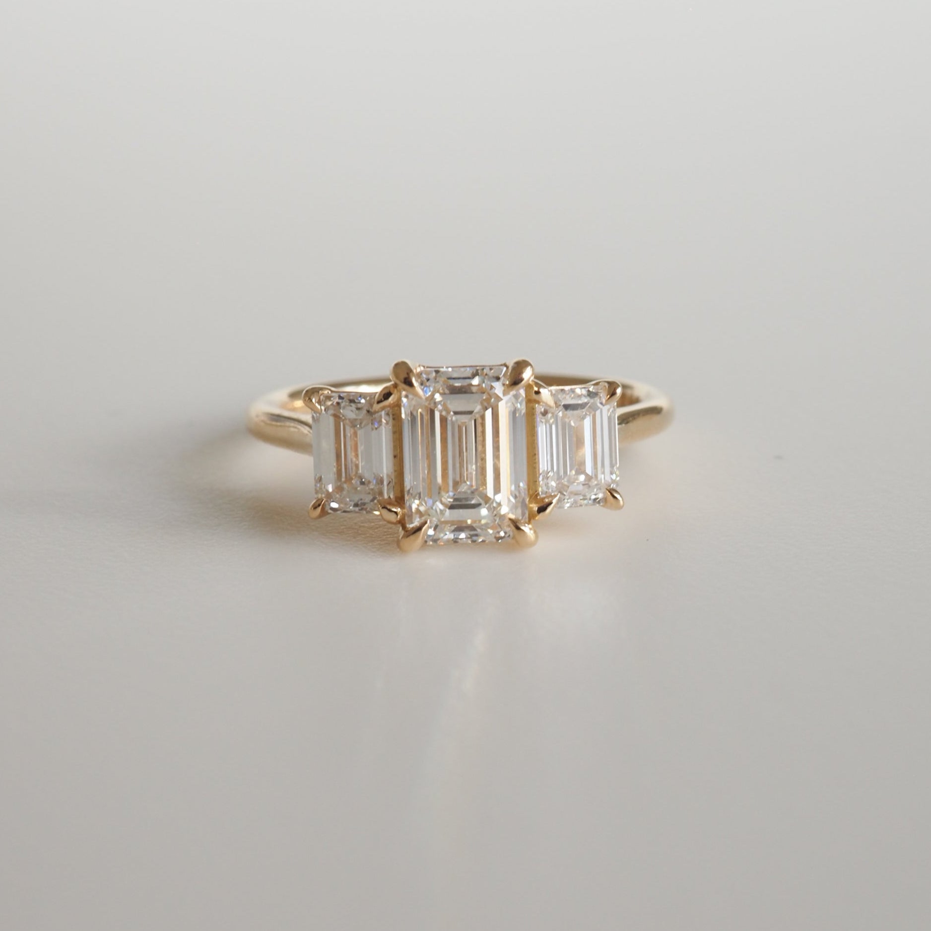 Emerald cut diamond ring in a gold setting, featuring three stones on a simple band, showcasing luxury jewellery design.