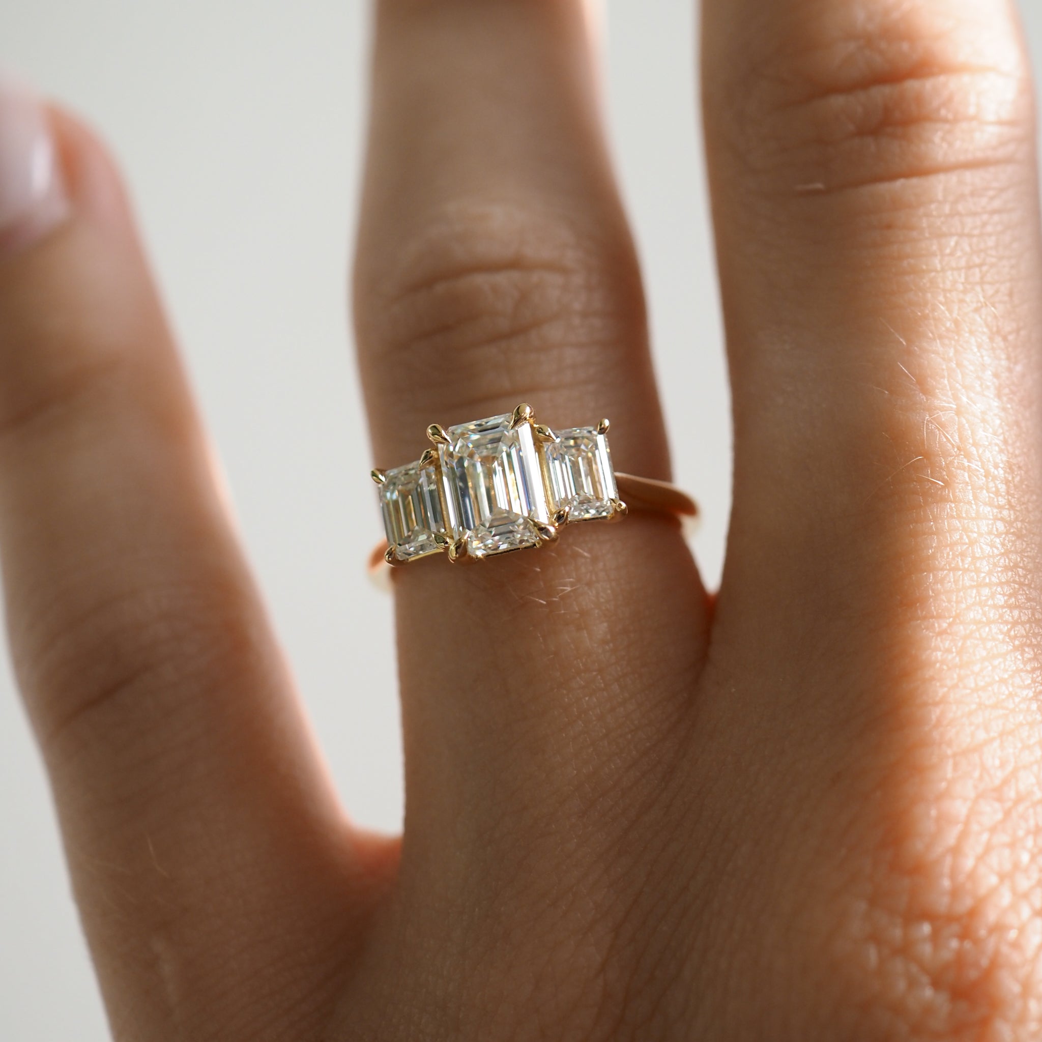 Hand wearing a gold ring with three emerald-cut diamonds in a row, showcasing luxury jewellery craftsmanship.