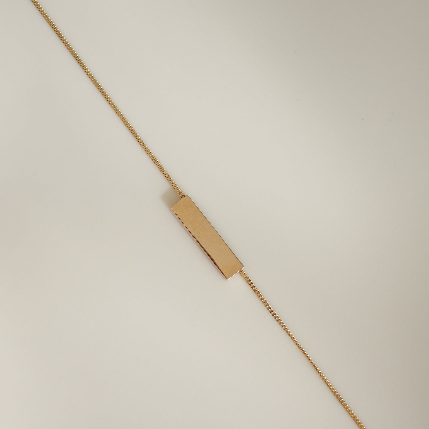 Gold bar bracelet on a thin, elegant chain against a neutral background, showcasing minimalist luxury jewellery design.