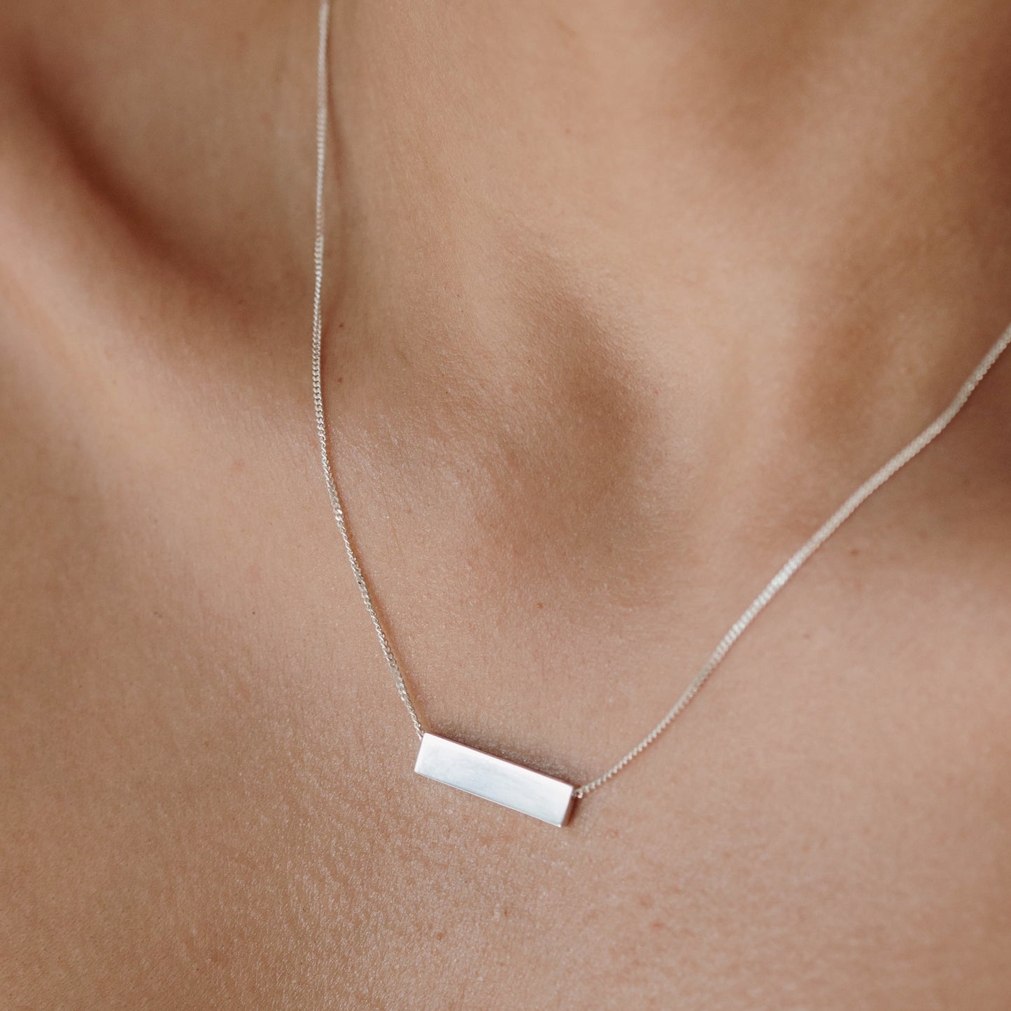 Elegant silver bar necklace on a woman's collarbone, showcasing minimalist luxury jewellery design.