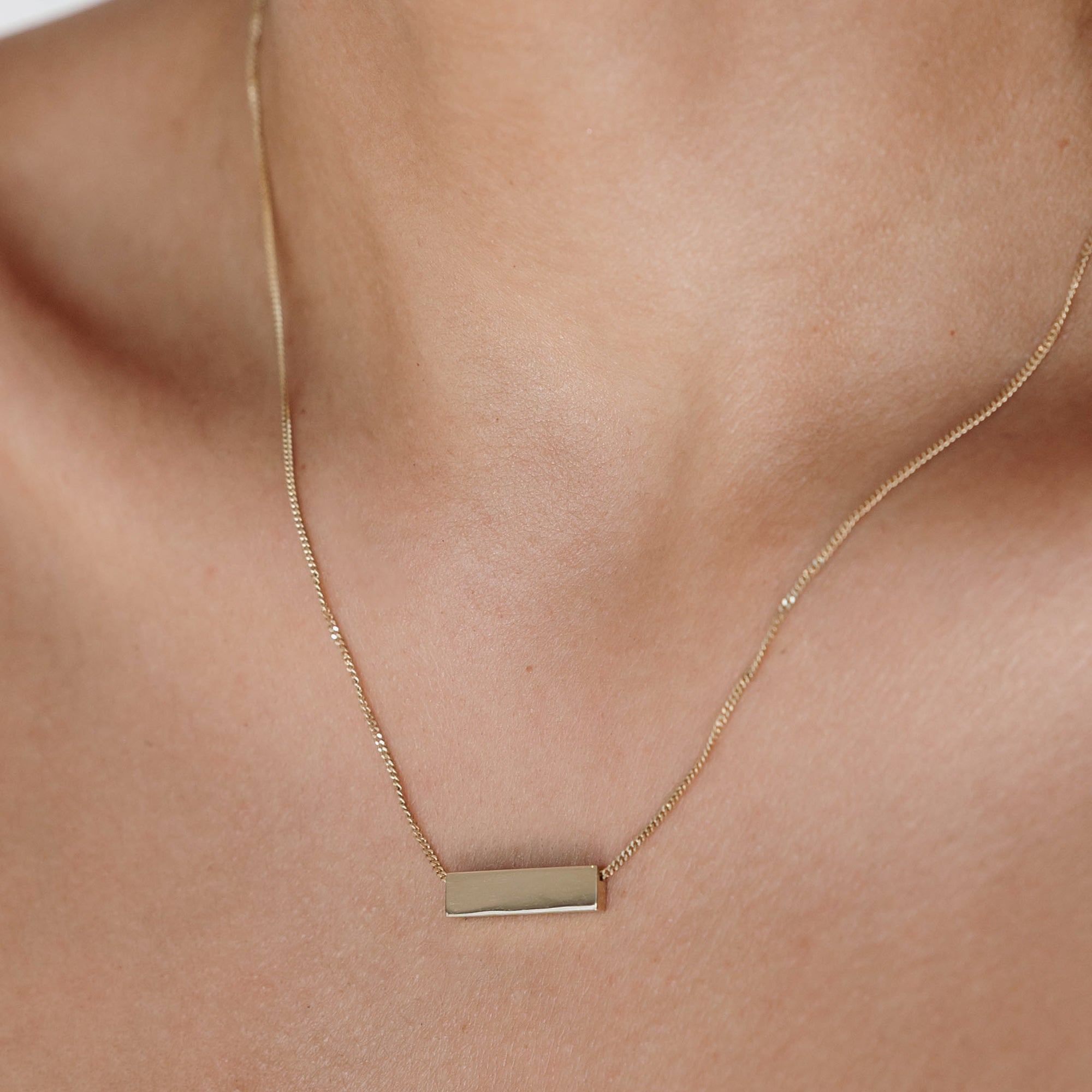 Close-up of a delicate gold necklace with a rectangular pendant on a woman's neck, showcasing elegant and minimalist jewellery design.