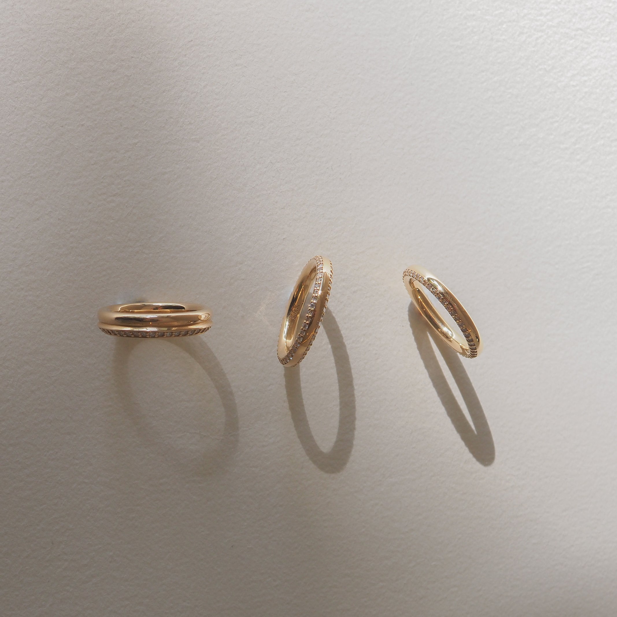 Three elegant gold hoop earrings with textured edges cast soft shadows on a beige surface, symbolising luxury jewellery design.