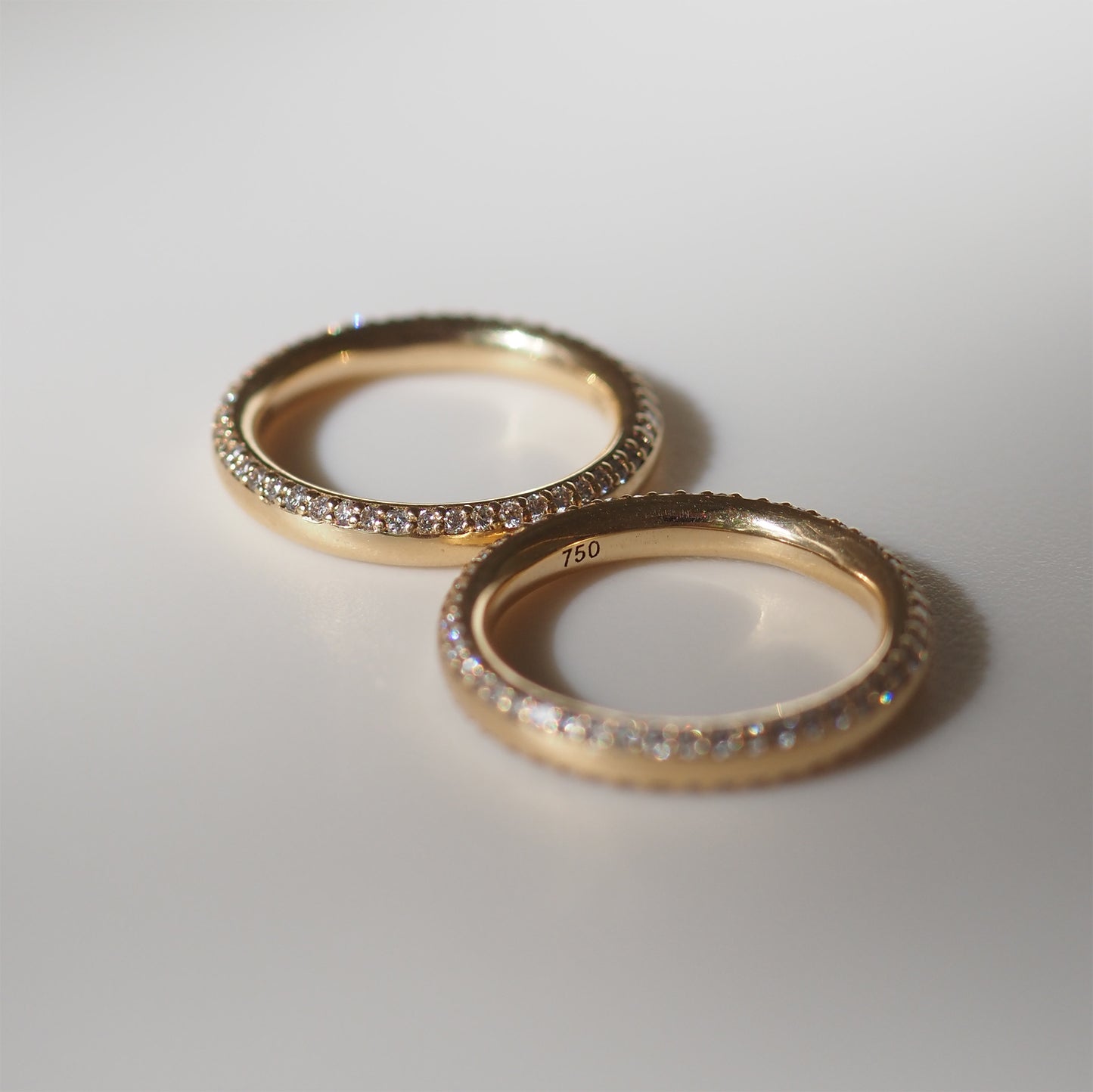 Two gold rings with diamond pavé detailing on a white background, marked "750" indicating 18k gold, symbolising luxury jewellery.